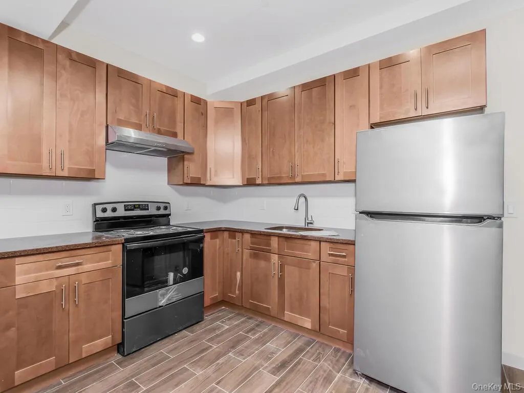 Kitchen with stainless steel appliances, brown cabinetry, wood tiled floors, dark stone counters, and recessed lighting Kitchen with stainless steel appliances, brown cabinetry, wood tiled floors, dark stone counters, and recessed lighting