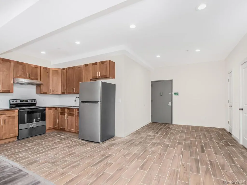 Kitchen featuring appliances with stainless steel finishes, brown cabinetry, recessed lighting, wood finish floors, and under cabinet range hood Kitchen featuring appliances with stainless steel finishes, brown cabinetry, recessed lighting, wood finish floors, and under cabinet range hood