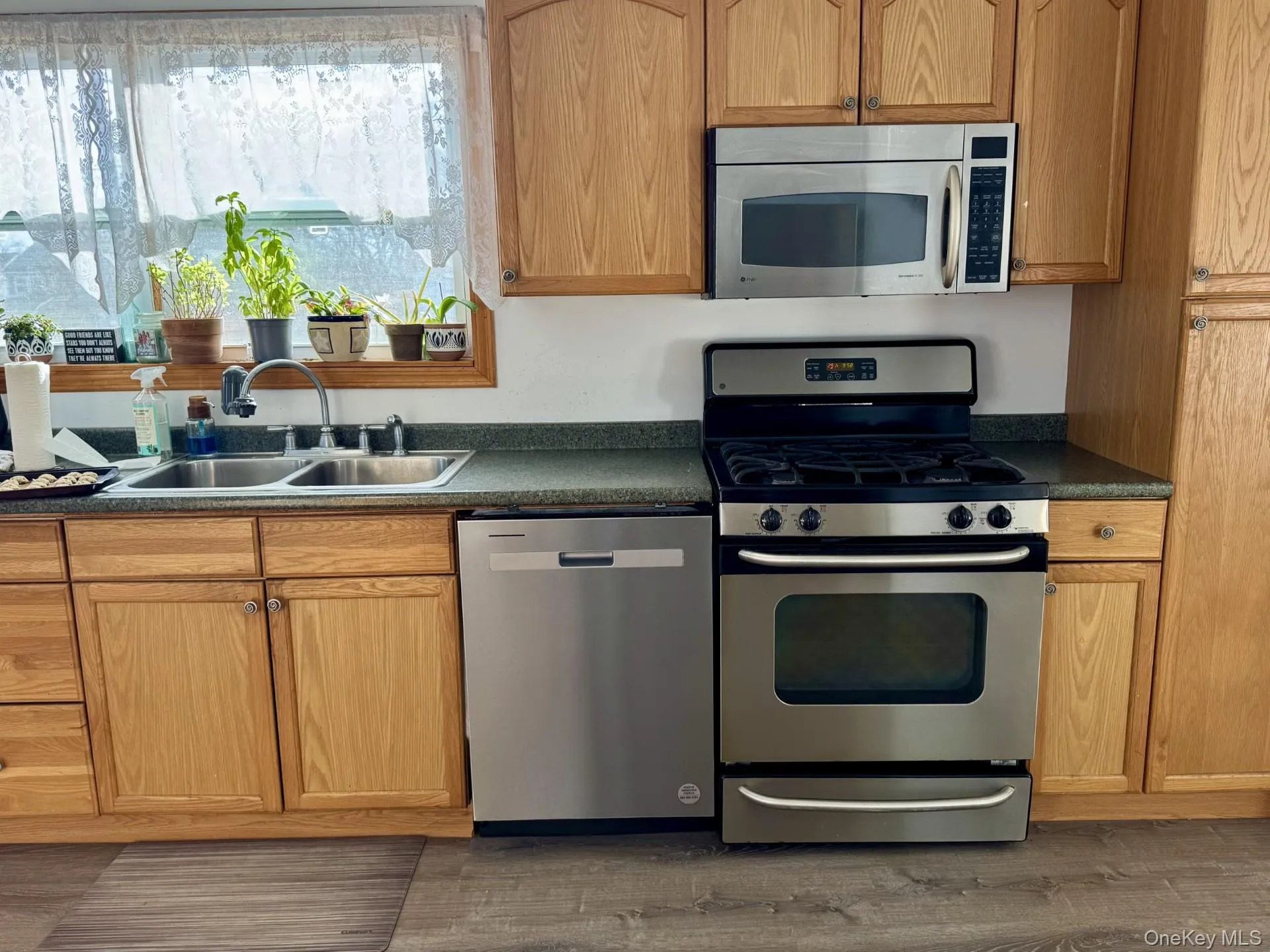 Kitchen with stainless steel appliances, dark countertops, dark wood-style flooring, and brown cabinets Kitchen with stainless steel appliances, dark countertops, dark wood-style flooring, and brown cabinets