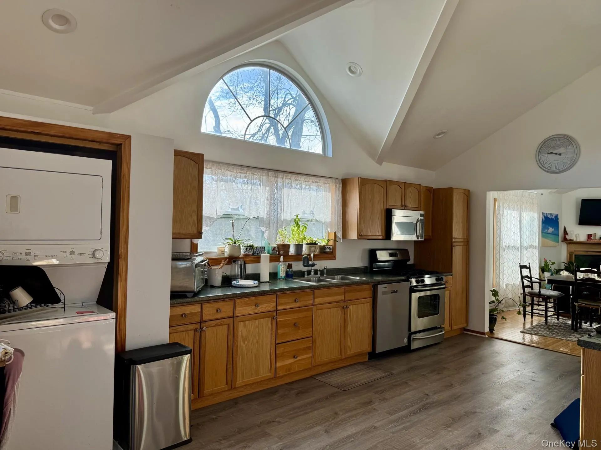 Kitchen with appliances with stainless steel finishes, dark countertops, dark wood-style floors, brown cabinets, and high vaulted ceiling Kitchen with appliances with stainless steel finishes, dark countertops, dark wood-style floors, brown cabinets, and high vaulted ceiling