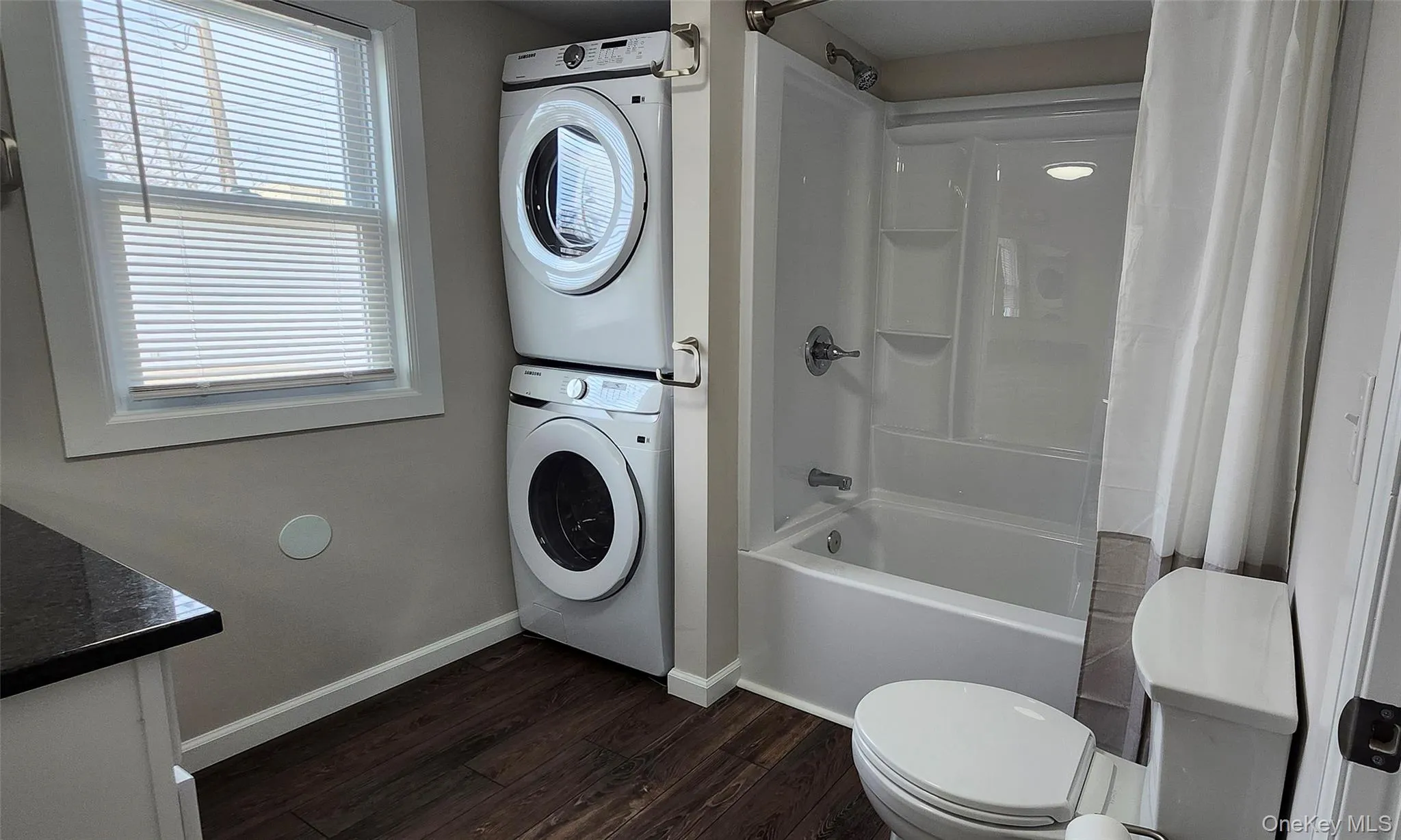 Bathroom featuring vanity, shower / bathtub combination with vinyl floors, and stacked washer and clothes dryer Bathroom featuring vanity, shower / bathtub combination with vinyl floors, and stacked washer and clothes dryer