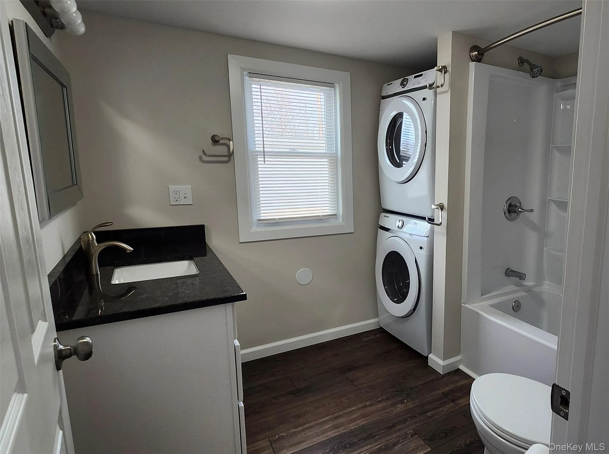 Full bathroom featuring vanity, shower / bathtub combination, vinyl floors and stacked washer and clothes dryer Full bathroom featuring vanity, shower / bathtub combination, vinyl floors and stacked washer and clothes dryer
