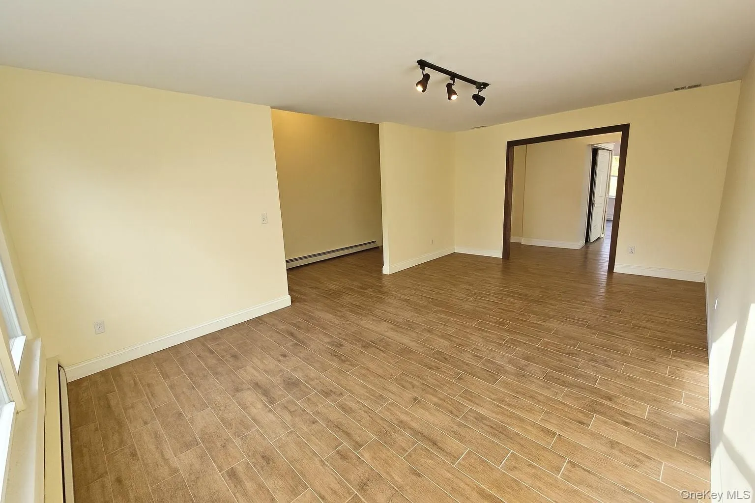 Empty room featuring track lighting, a baseboard heating unit, and wood finish floors Empty room featuring track lighting, a baseboard heating unit, and wood finish floors