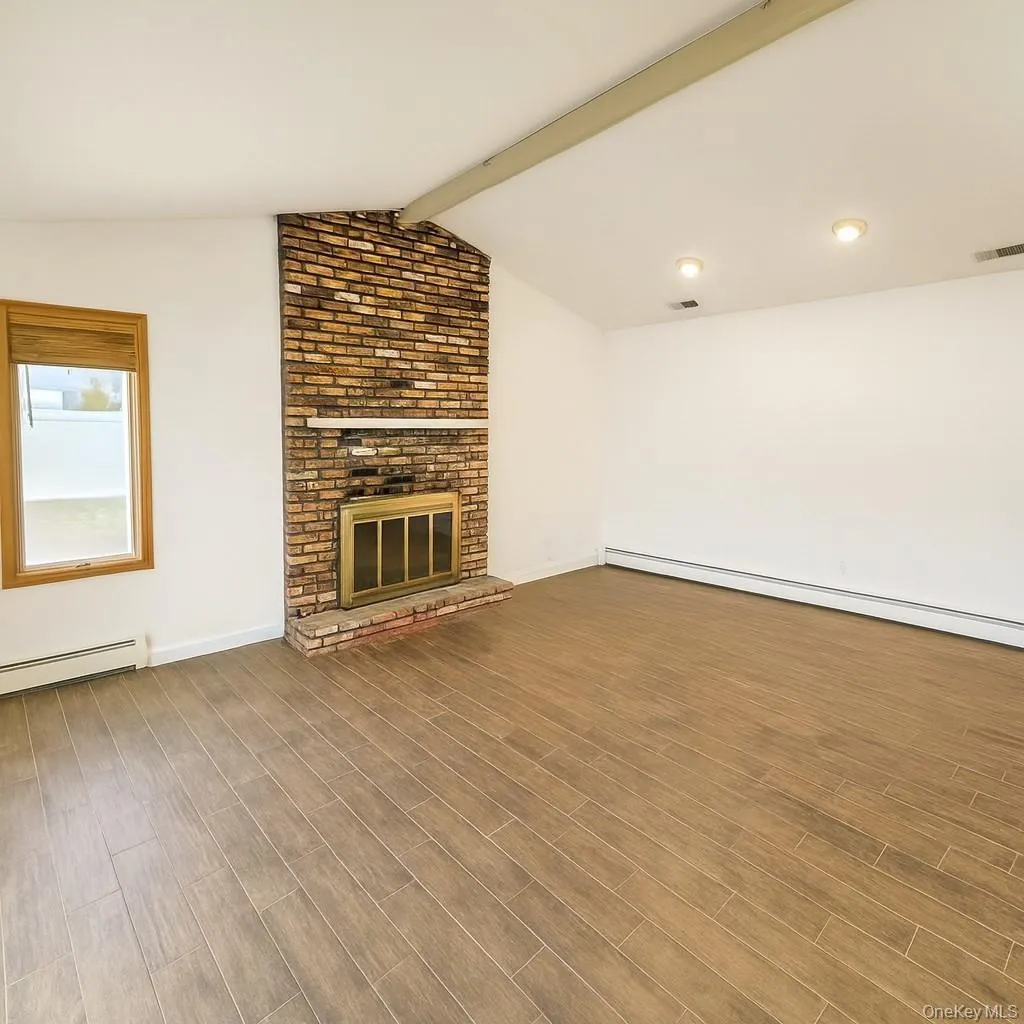 Unfurnished living room featuring a brick fireplace, wood finished floors, and a baseboard radiator Unfurnished living room featuring a brick fireplace, wood finished floors, and a baseboard radiator