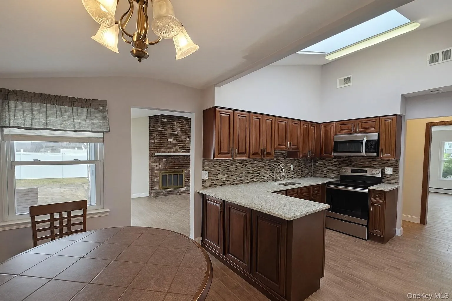 Kitchen with appliances with stainless steel finishes, a peninsula, vaulted ceiling, light wood finished floors, and a brick fireplace Kitchen with appliances with stainless steel finishes, a peninsula, vaulted ceiling, light wood finished floors, and a brick fireplace