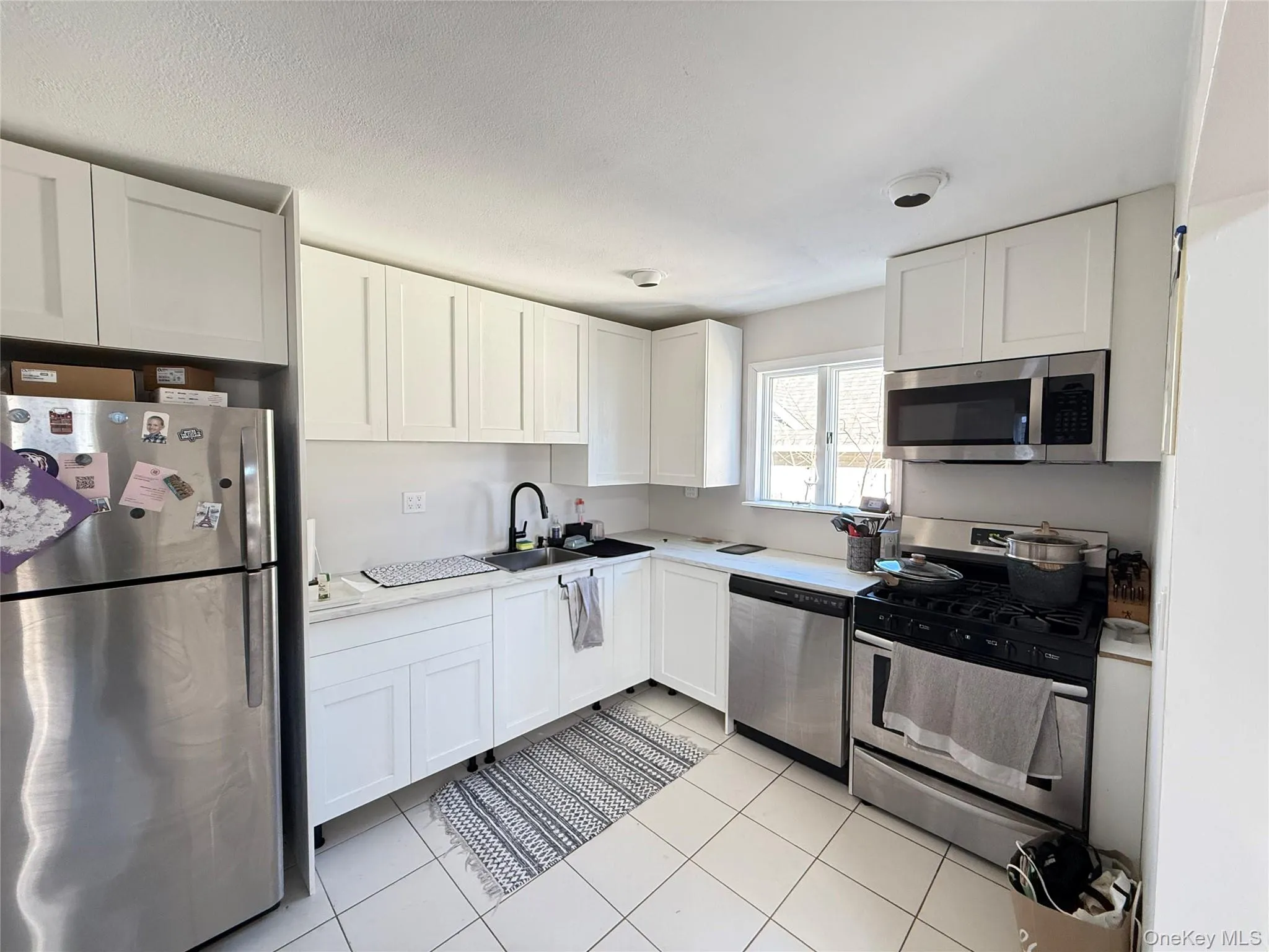 Kitchen with appliances with stainless steel finishes, white cabinets, light tile patterned floors, and a textured ceiling Kitchen with appliances with stainless steel finishes, white cabinets, light tile patterned floors, and a textured ceiling