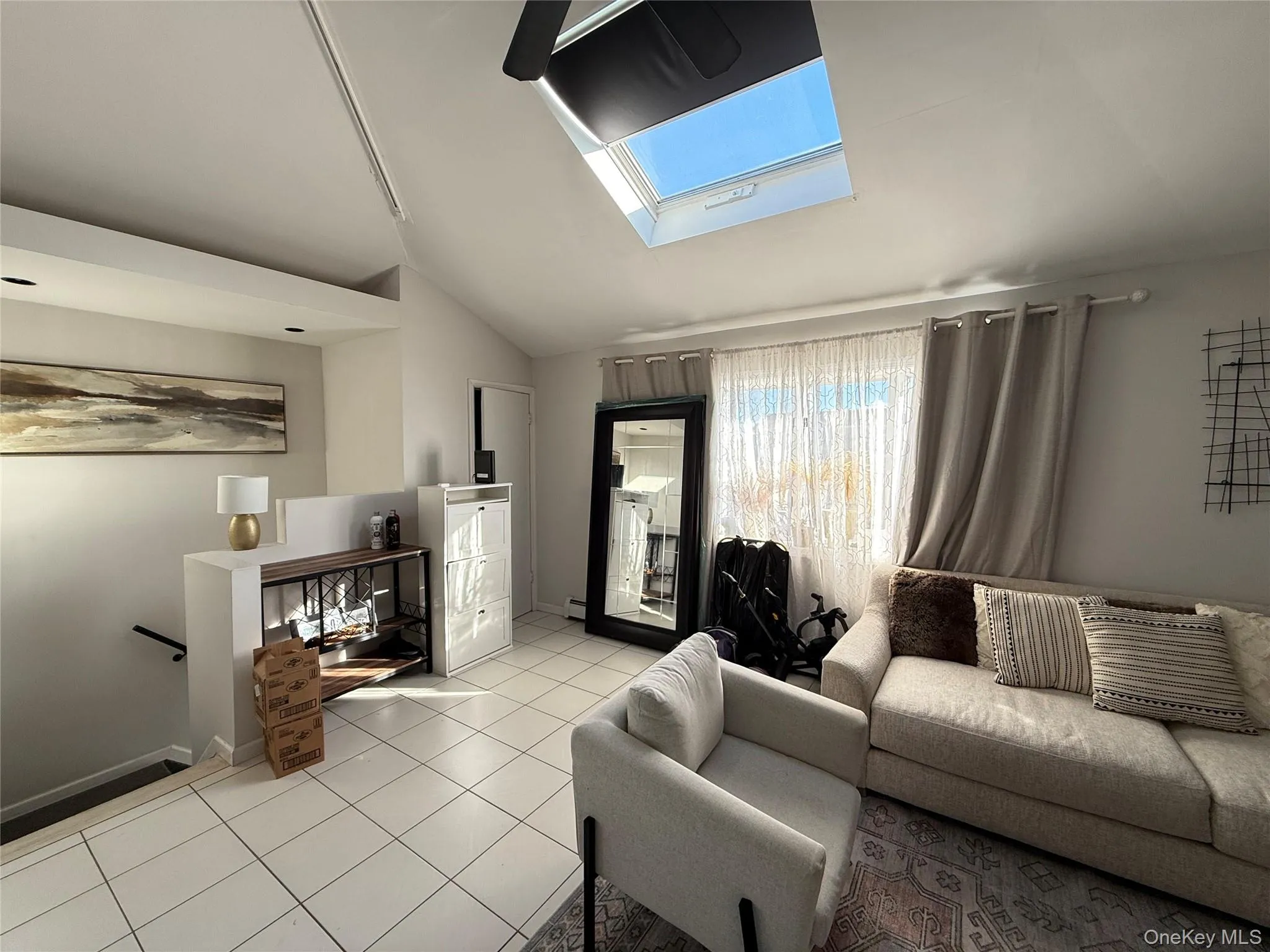Living area featuring vaulted ceiling, a skylight, and tile patterned floors Living area featuring vaulted ceiling, a skylight, and tile patterned floors