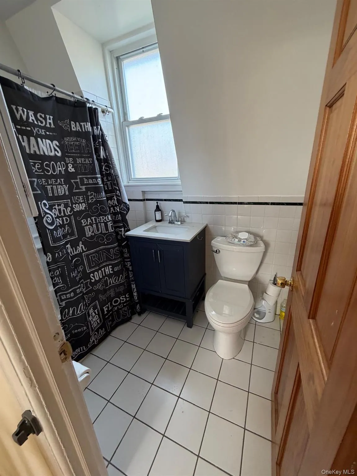 Full bathroom featuring light tile patterned floors, vanity, a wainscoted wall, a shower with curtain, and tile walls Full bathroom featuring light tile patterned floors, vanity, a wainscoted wall, a shower with curtain, and tile walls
