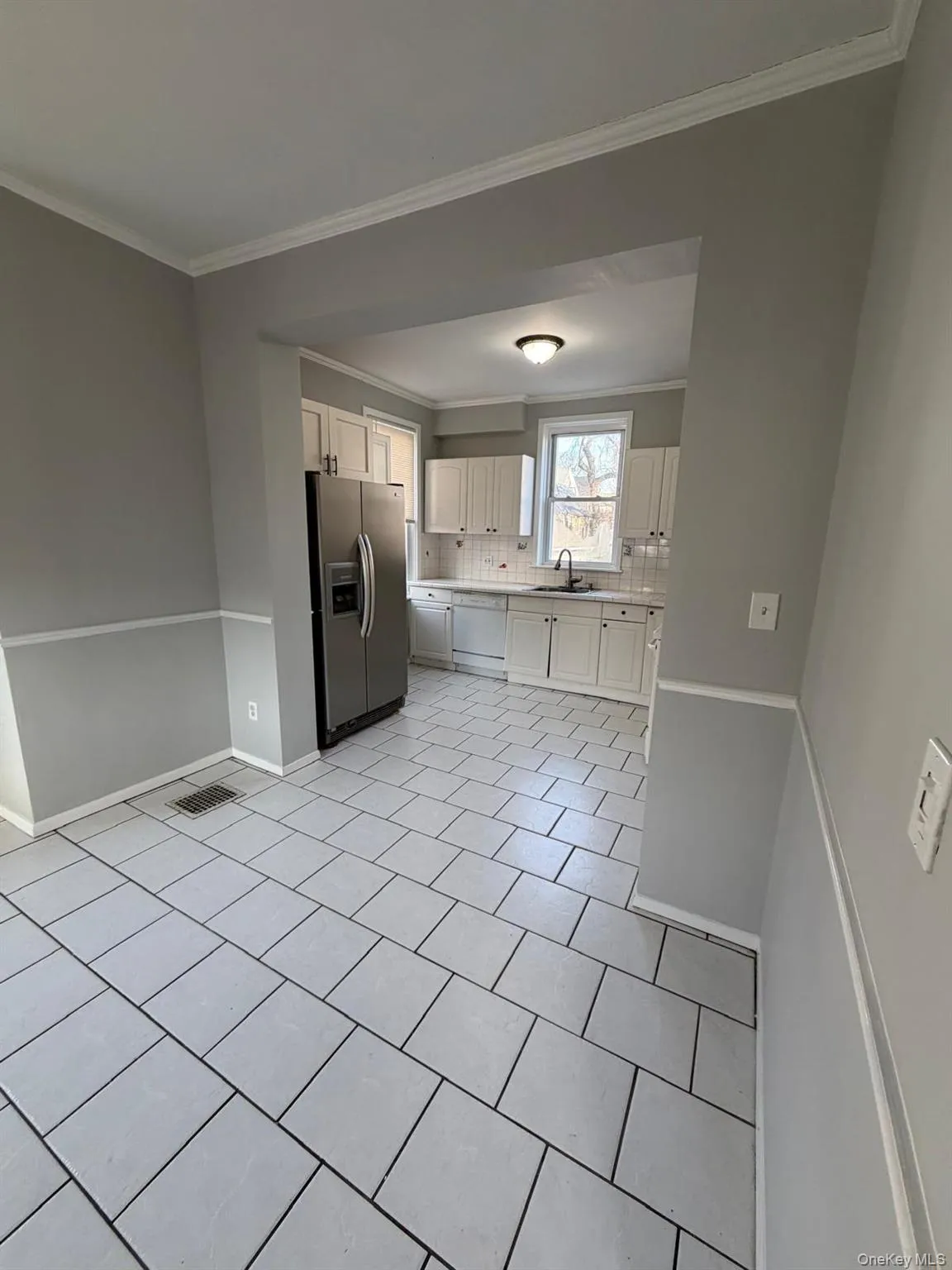 Kitchen with tasteful backsplash, stainless steel fridge with ice dispenser, light countertops, white cabinets, and light tile patterned floors Kitchen with tasteful backsplash, stainless steel fridge with ice dispenser, light countertops, white cabinets, and light tile patterned floors