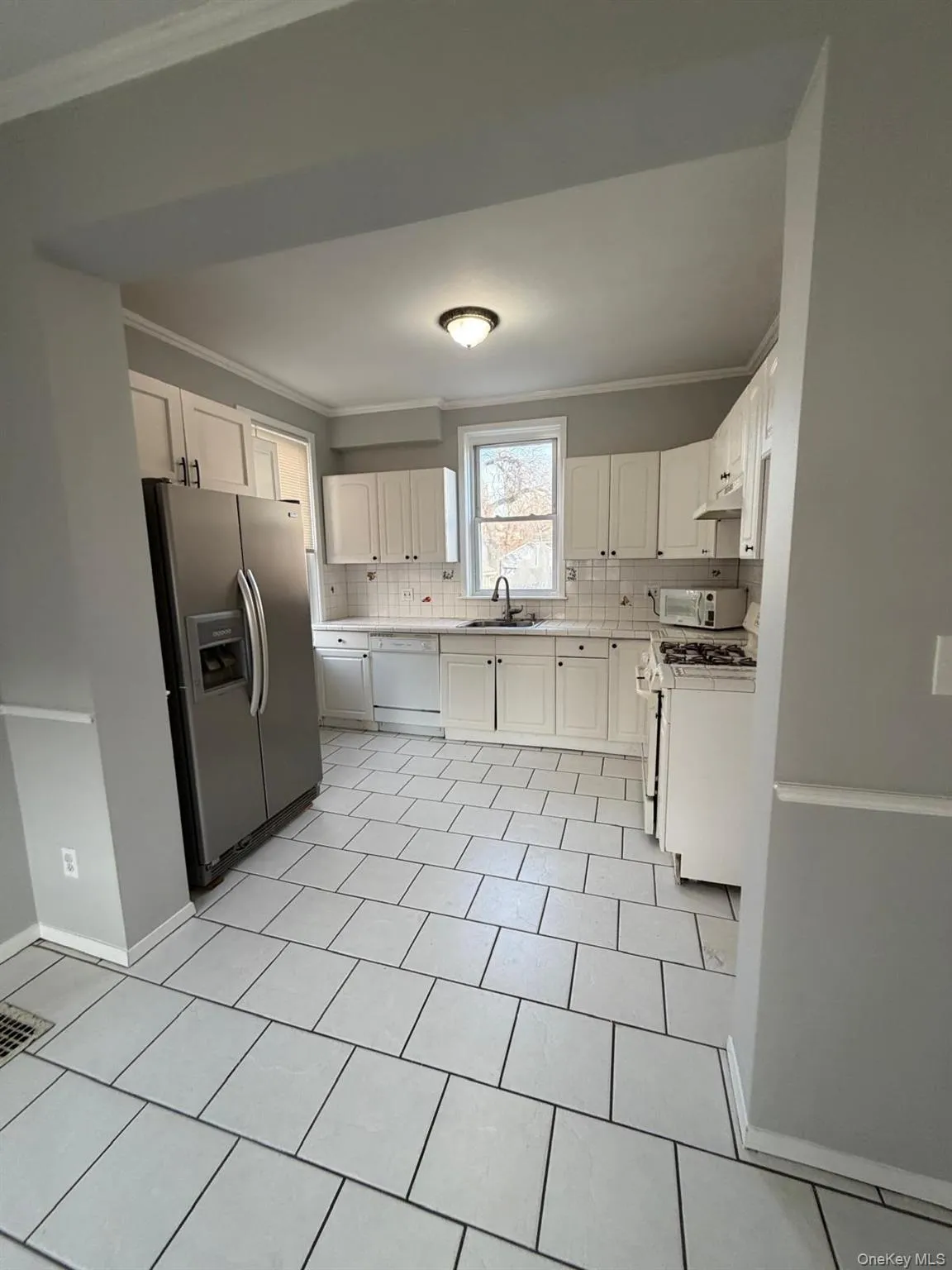 Kitchen with white cabinetry, white appliances, crown molding, backsplash, and light tile patterned flooring Kitchen with white cabinetry, white appliances, crown molding, backsplash, and light tile patterned flooring