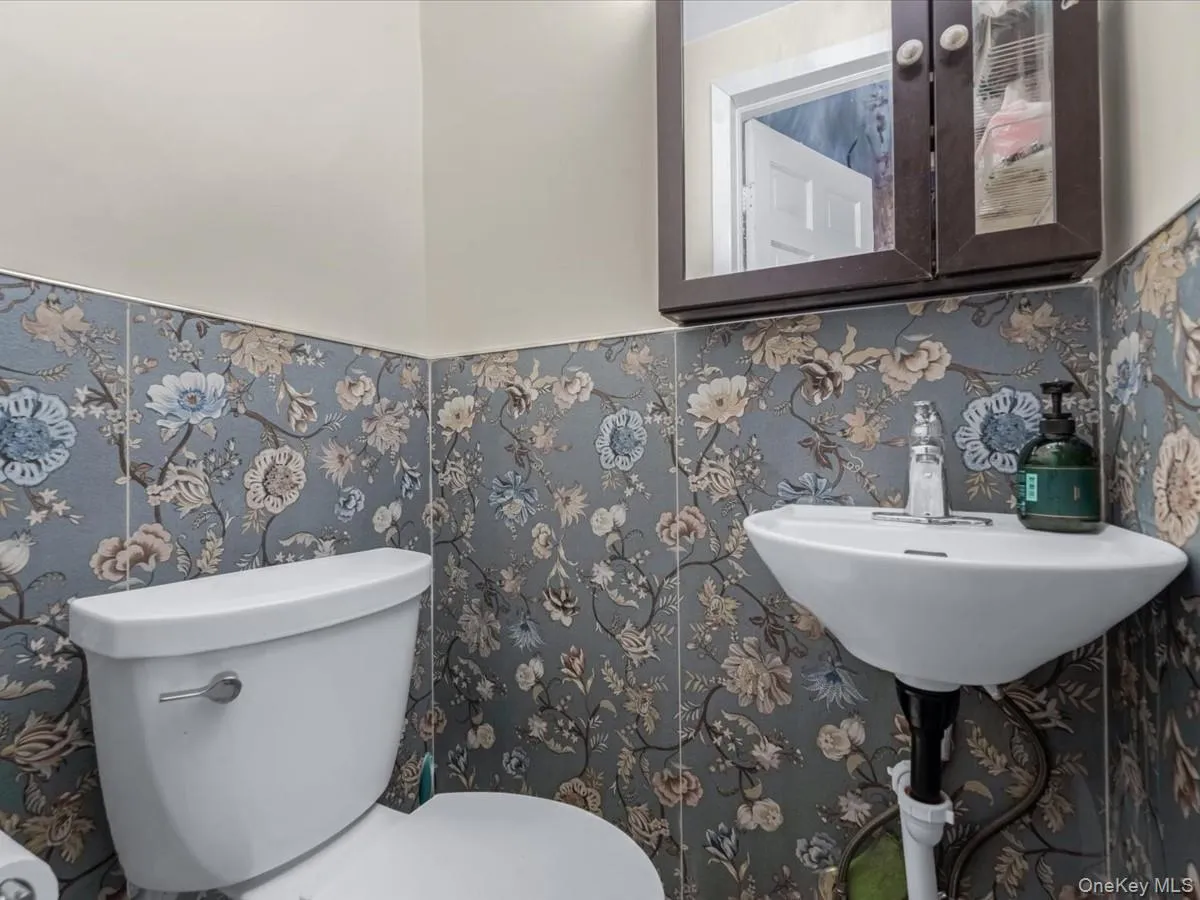 Half bathroom featuring wallpapered walls and wainscoting Half bathroom featuring wallpapered walls and wainscoting