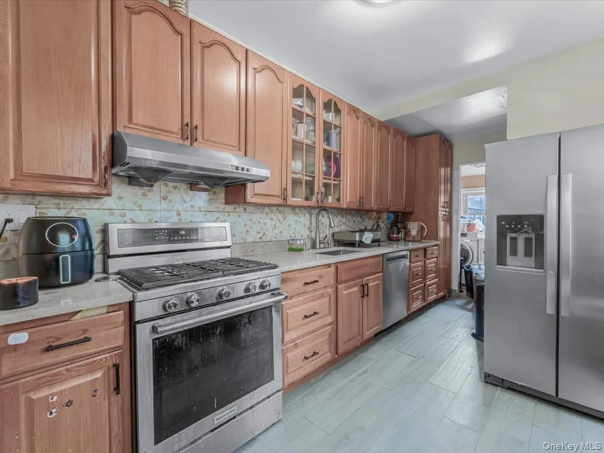 Kitchen with stainless steel appliances, under cabinet range hood, backsplash, glass insert cabinets, and light stone countertops Kitchen with stainless steel appliances, under cabinet range hood, backsplash, glass insert cabinets, and light stone countertops