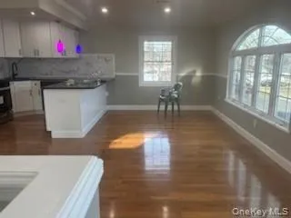 Kitchen with white cabinetry, dark wood-style flooring, tasteful backsplash, dark countertops, and black stove Kitchen with white cabinetry, dark wood-style flooring, tasteful backsplash, dark countertops, and black stove