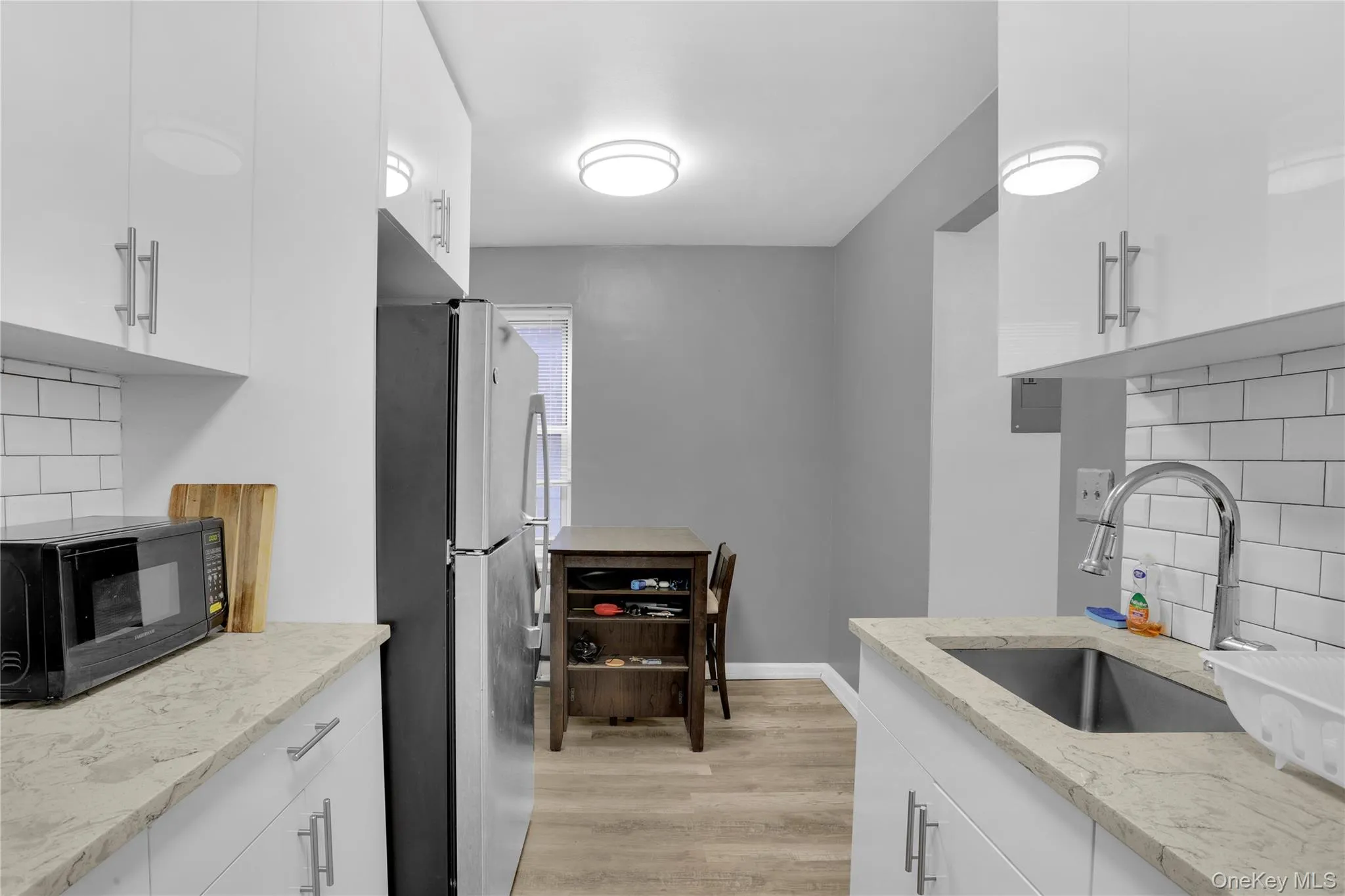 Kitchen featuring tasteful backsplash, white cabinets, freestanding refrigerator, and light stone countertops Kitchen featuring tasteful backsplash, white cabinets, freestanding refrigerator, and light stone countertops