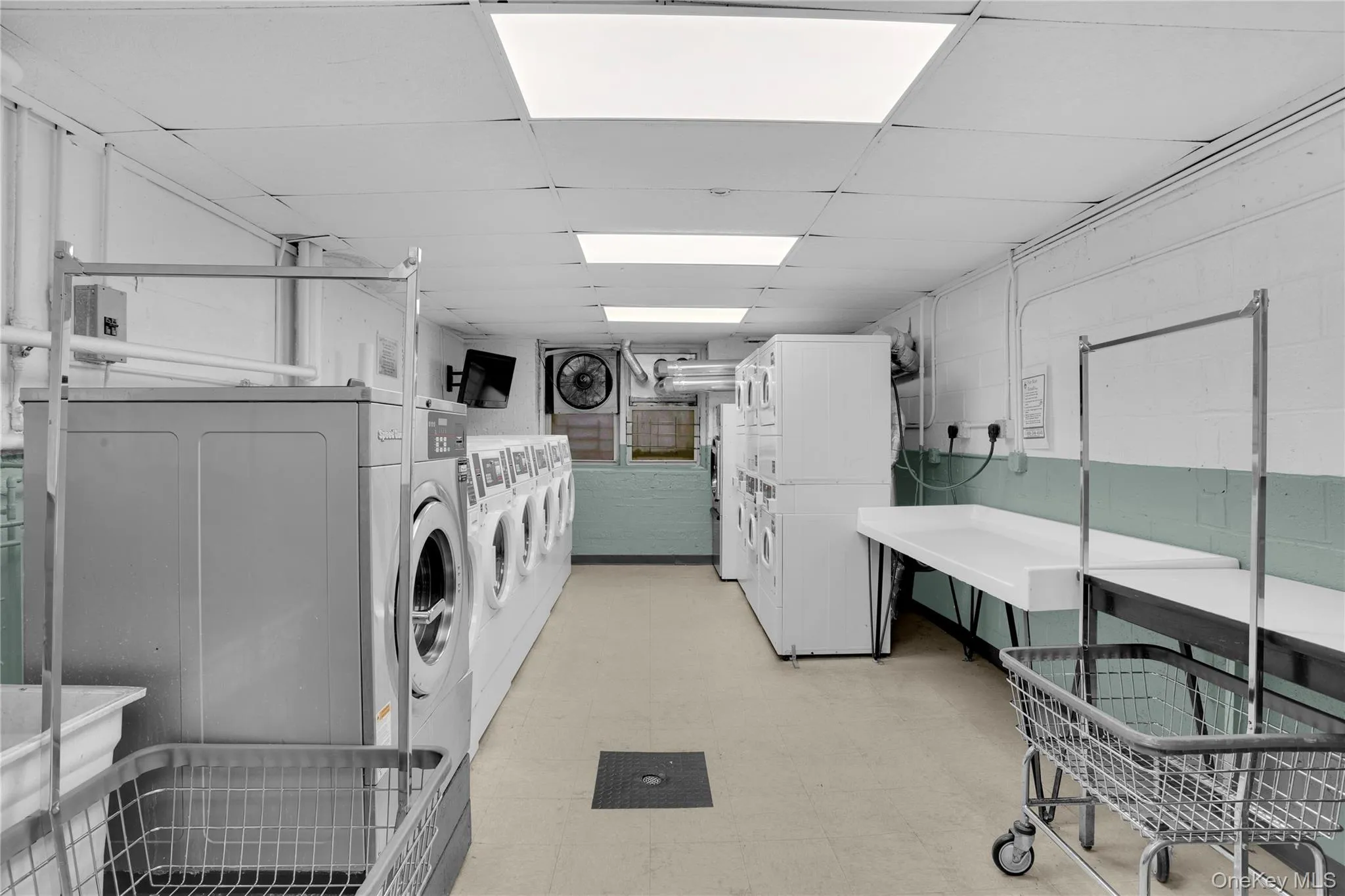 Community laundry featuring light floors, a paneled ceiling, estacked washer and dryer, concrete block wall, and independent washer and dryer Community laundry featuring light floors, a paneled ceiling, estacked washer and dryer, concrete block wall, and independent washer and dryer
