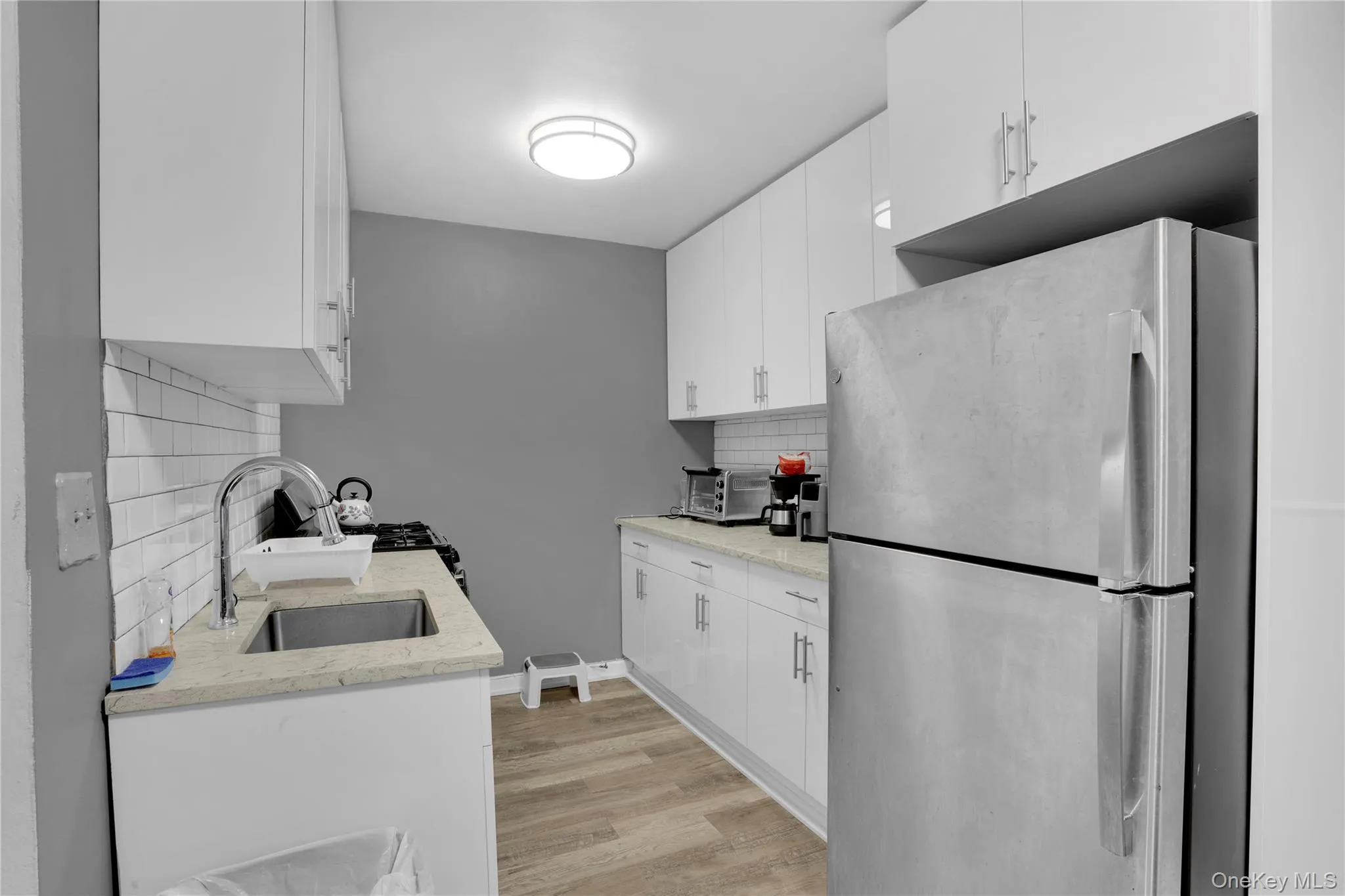 Kitchen with freestanding refrigerator, white cabinetry, tasteful backsplash, and light stone counters Kitchen with freestanding refrigerator, white cabinetry, tasteful backsplash, and light stone counters