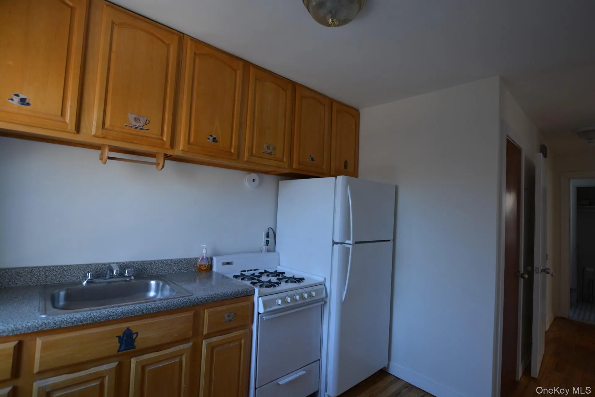 Kitchen with dark countertops, white appliances, brown cabinets, and dark wood-style flooring Kitchen with dark countertops, white appliances, brown cabinets, and dark wood-style flooring