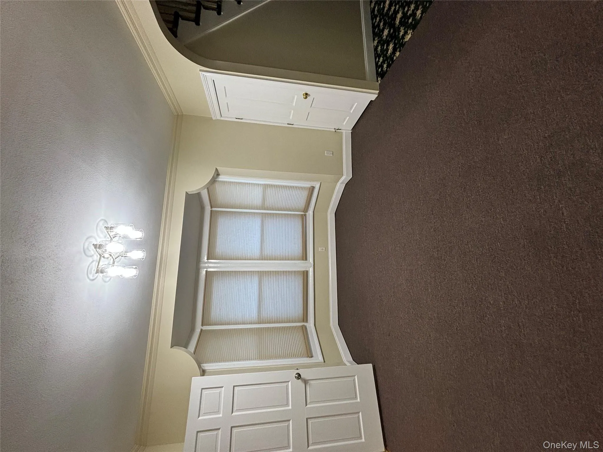 Empty room with a textured ceiling, ornamental molding, arched walkways, dark colored carpet, and stairway Empty room with a textured ceiling, ornamental molding, arched walkways, dark colored carpet, and stairway