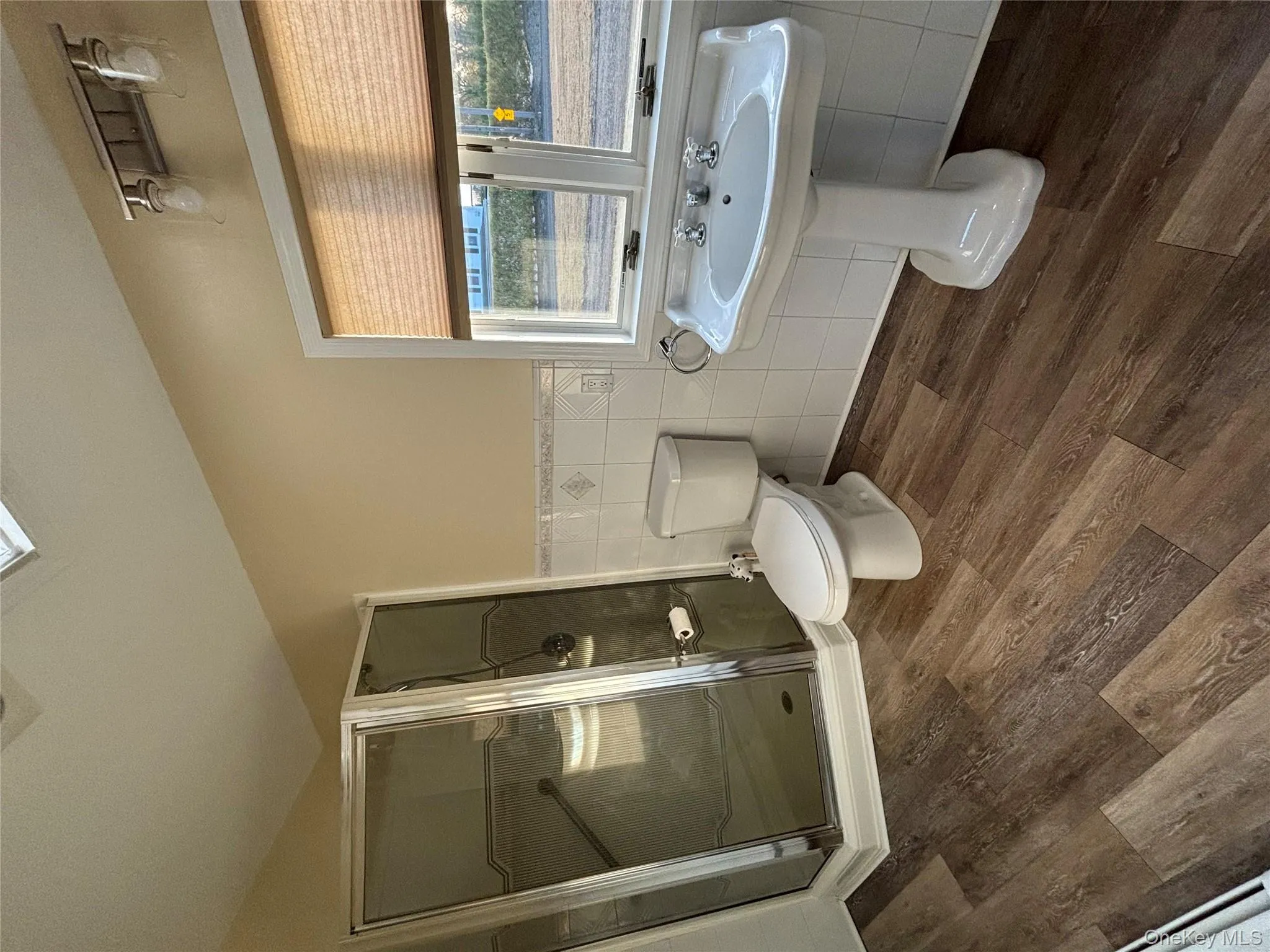 Full bath featuring a shower stall, tile walls, a wainscoted wall, and dark wood-style floors Full bath featuring a shower stall, tile walls, a wainscoted wall, and dark wood-style floors