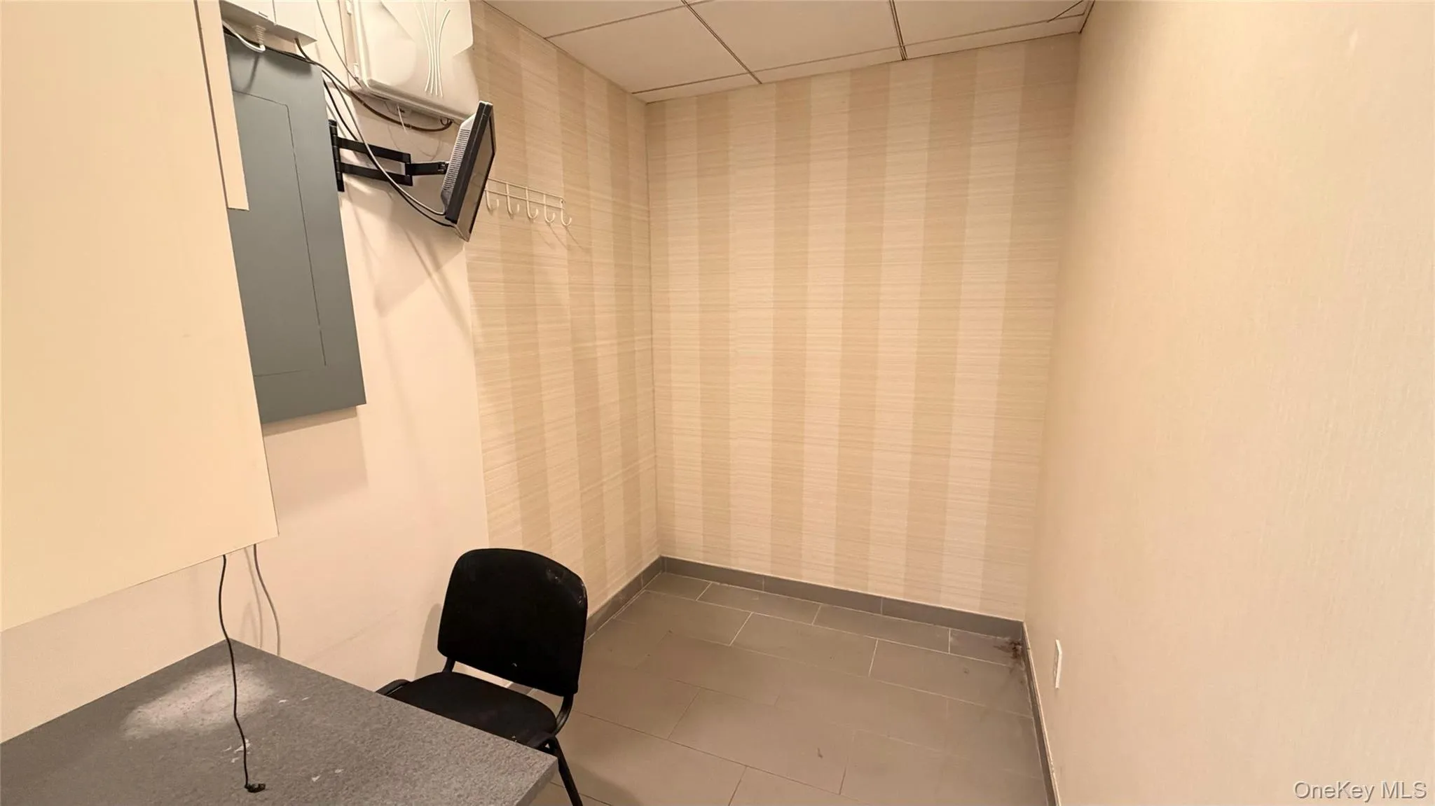 Office area with electric panel, a drop ceiling, dark tile patterned floors, and wallpapered walls Office area with electric panel, a drop ceiling, dark tile patterned floors, and wallpapered walls