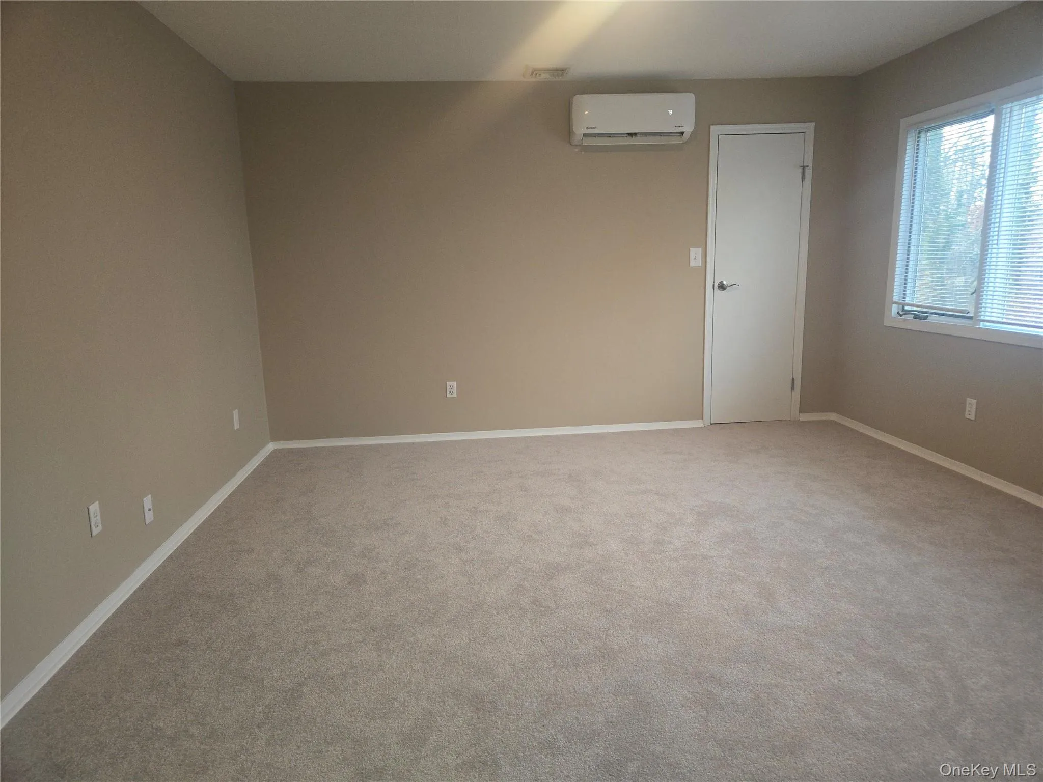 Spare room featuring a wall mounted air conditioner and light colored carpet Spare room featuring a wall mounted air conditioner and light colored carpet