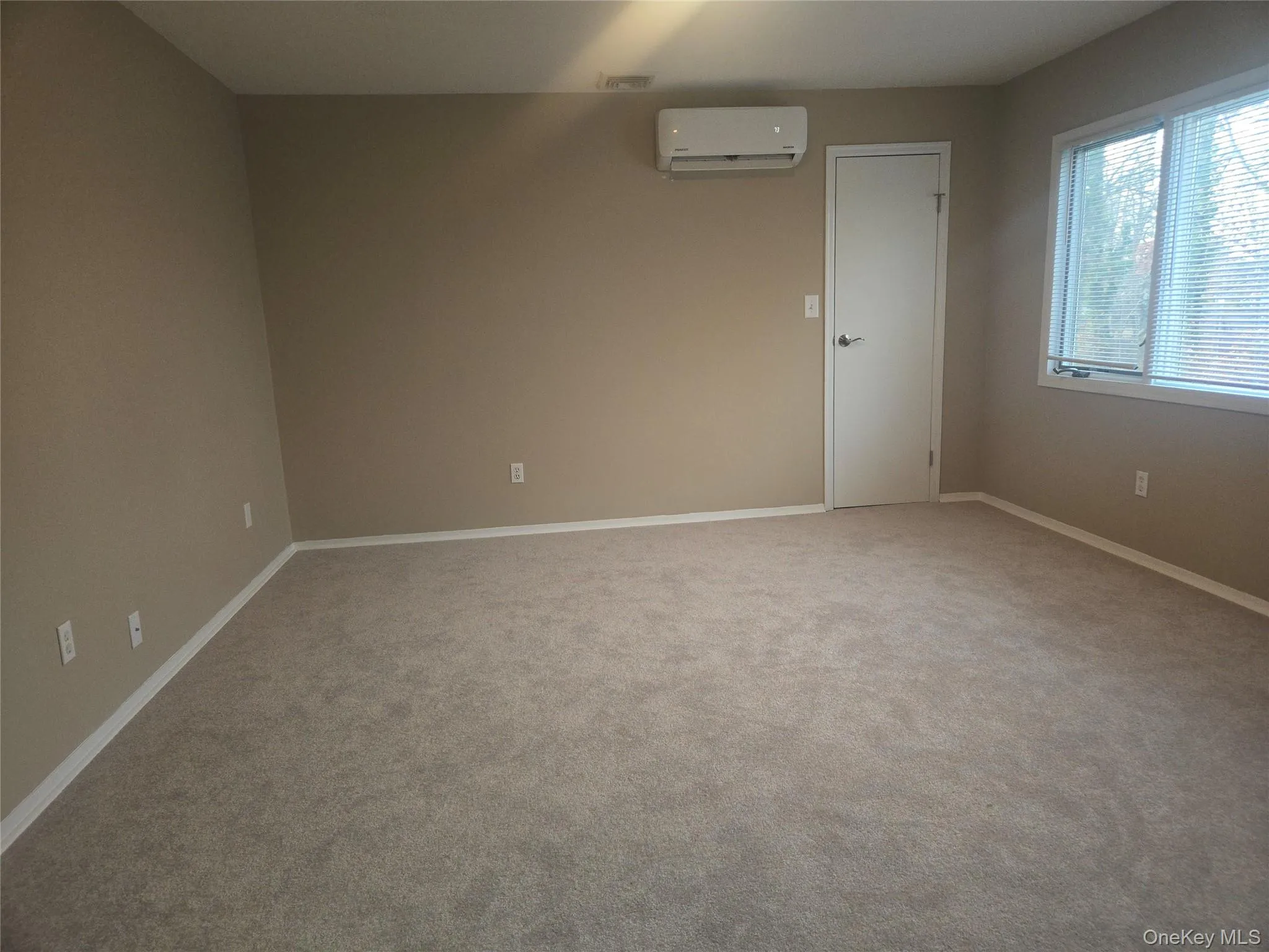 Empty room with light carpet and a wall mounted AC Empty room with light carpet and a wall mounted AC