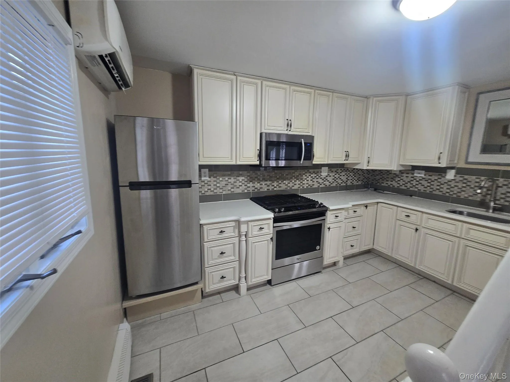 Kitchen featuring stainless steel appliances, a wall unit AC, light tile patterned flooring, backsplash, and light stone countertops Kitchen featuring stainless steel appliances, a wall unit AC, light tile patterned flooring, backsplash, and light stone countertops