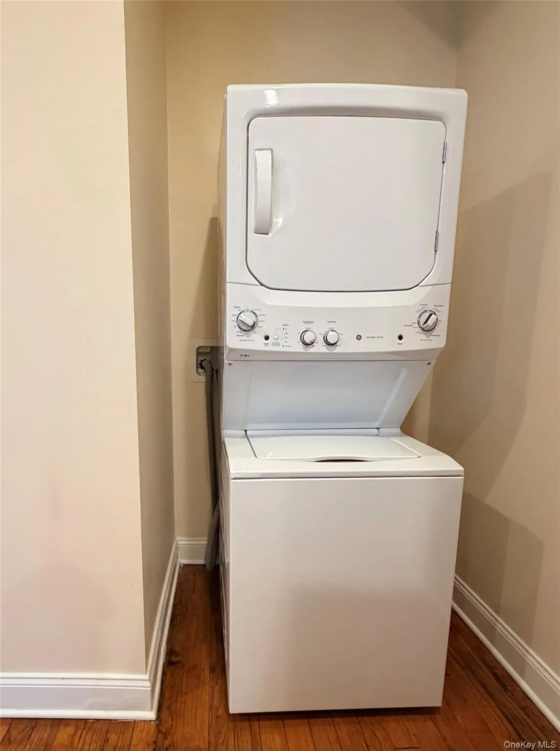 Washroom featuring stacked washer / drying machine and dark wood-style flooring Washroom featuring stacked washer / drying machine and dark wood-style flooring