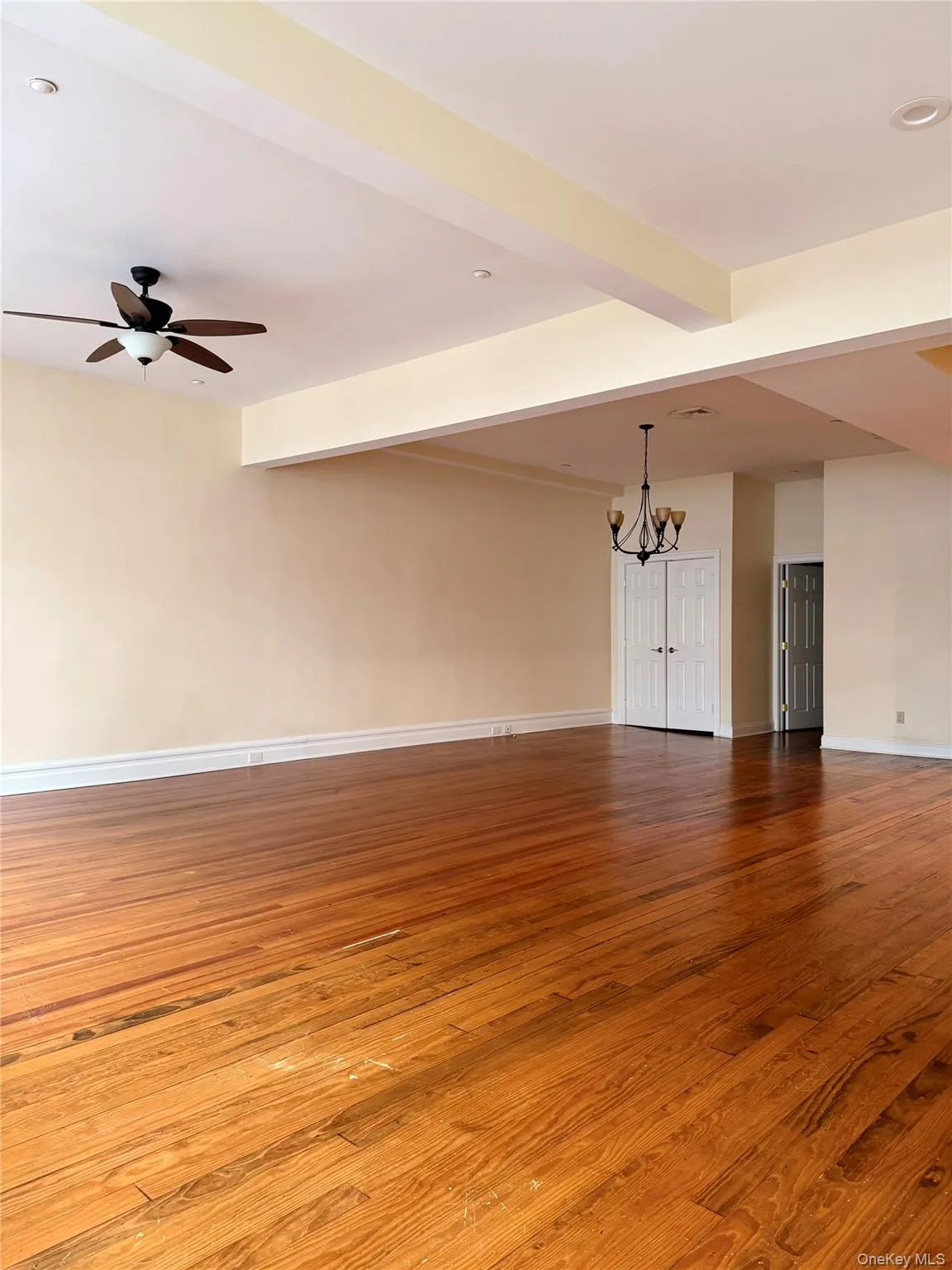 Unfurnished living room featuring a chandelier, beam ceiling, light wood-style flooring, and a ceiling fan Unfurnished living room featuring a chandelier, beam ceiling, light wood-style flooring, and a ceiling fan