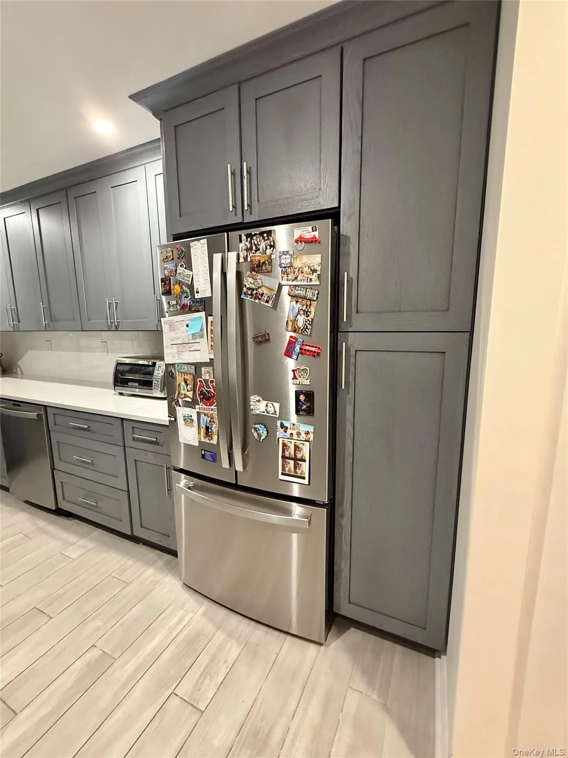 Kitchen featuring stainless steel appliances, gray cabinets, wood finish floors, decorative backsplash, and light stone counters Kitchen featuring stainless steel appliances, gray cabinets, wood finish floors, decorative backsplash, and light stone counters