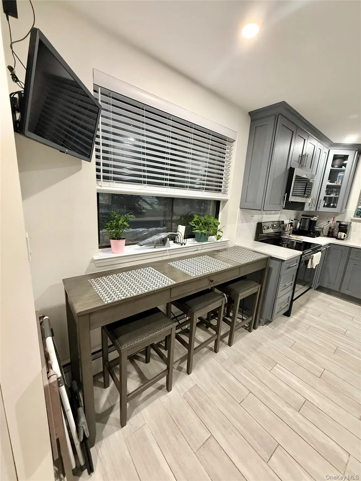 Kitchen with gray cabinets, electric stove, light wood finished floors, backsplash, and glass insert cabinets Kitchen with gray cabinets, electric stove, light wood finished floors, backsplash, and glass insert cabinets