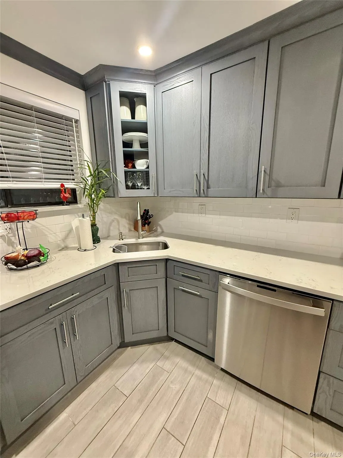 Kitchen with gray cabinetry, dishwasher, light stone counters, tasteful backsplash, and glass insert cabinets Kitchen with gray cabinetry, dishwasher, light stone counters, tasteful backsplash, and glass insert cabinets