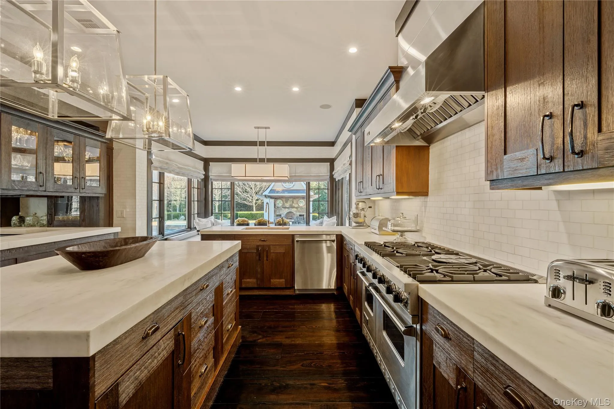Kitchen with stainless steel appliances, range hood, pendant lighting, dark wood-type flooring, and glass insert cabinets Kitchen with stainless steel appliances, range hood, pendant lighting, dark wood-type flooring, and glass insert cabinets