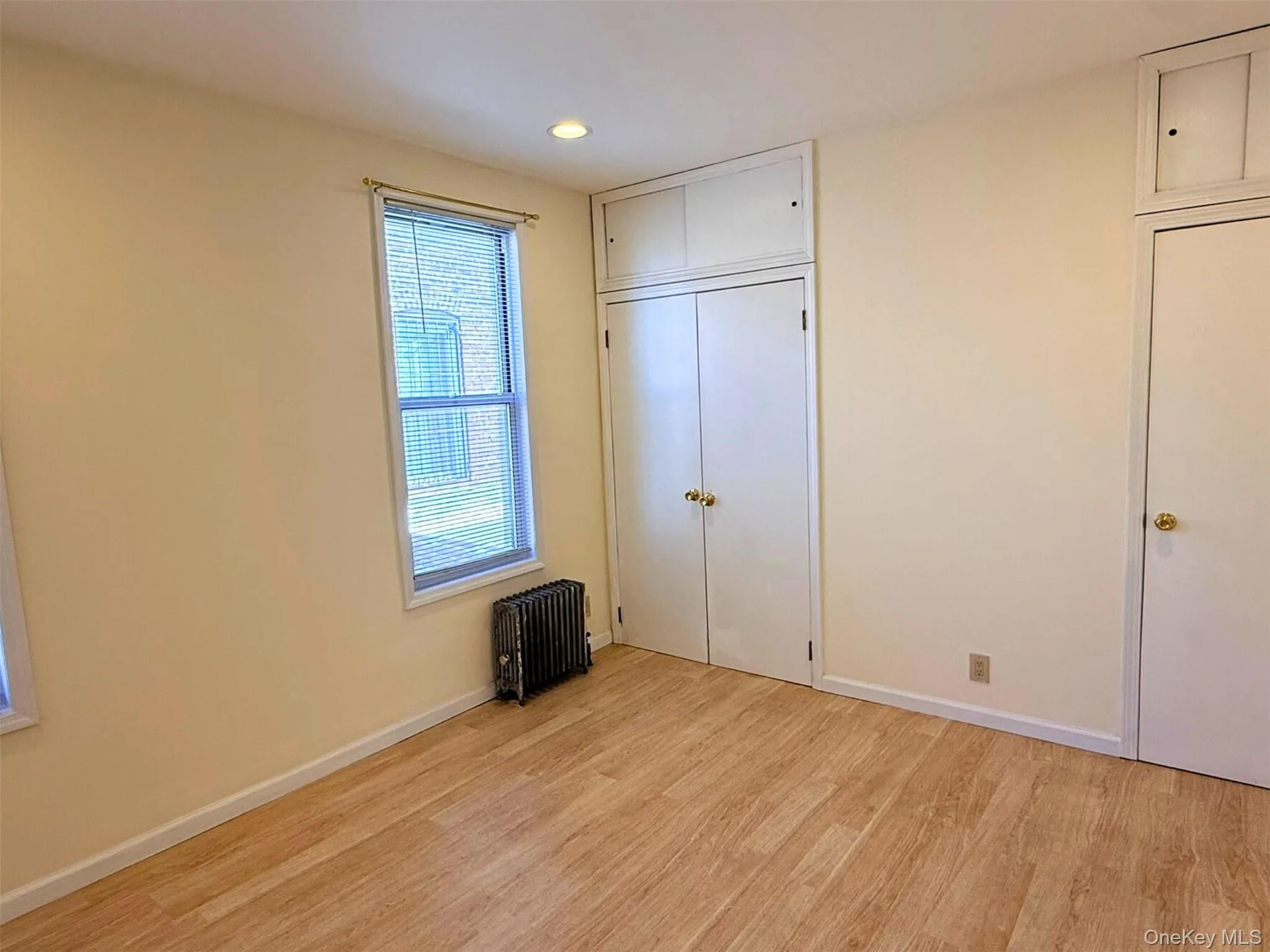 Unfurnished bedroom with light wood-style flooring, radiator heating unit, a closet, and recessed lighting Unfurnished bedroom with light wood-style flooring, radiator heating unit, a closet, and recessed lighting