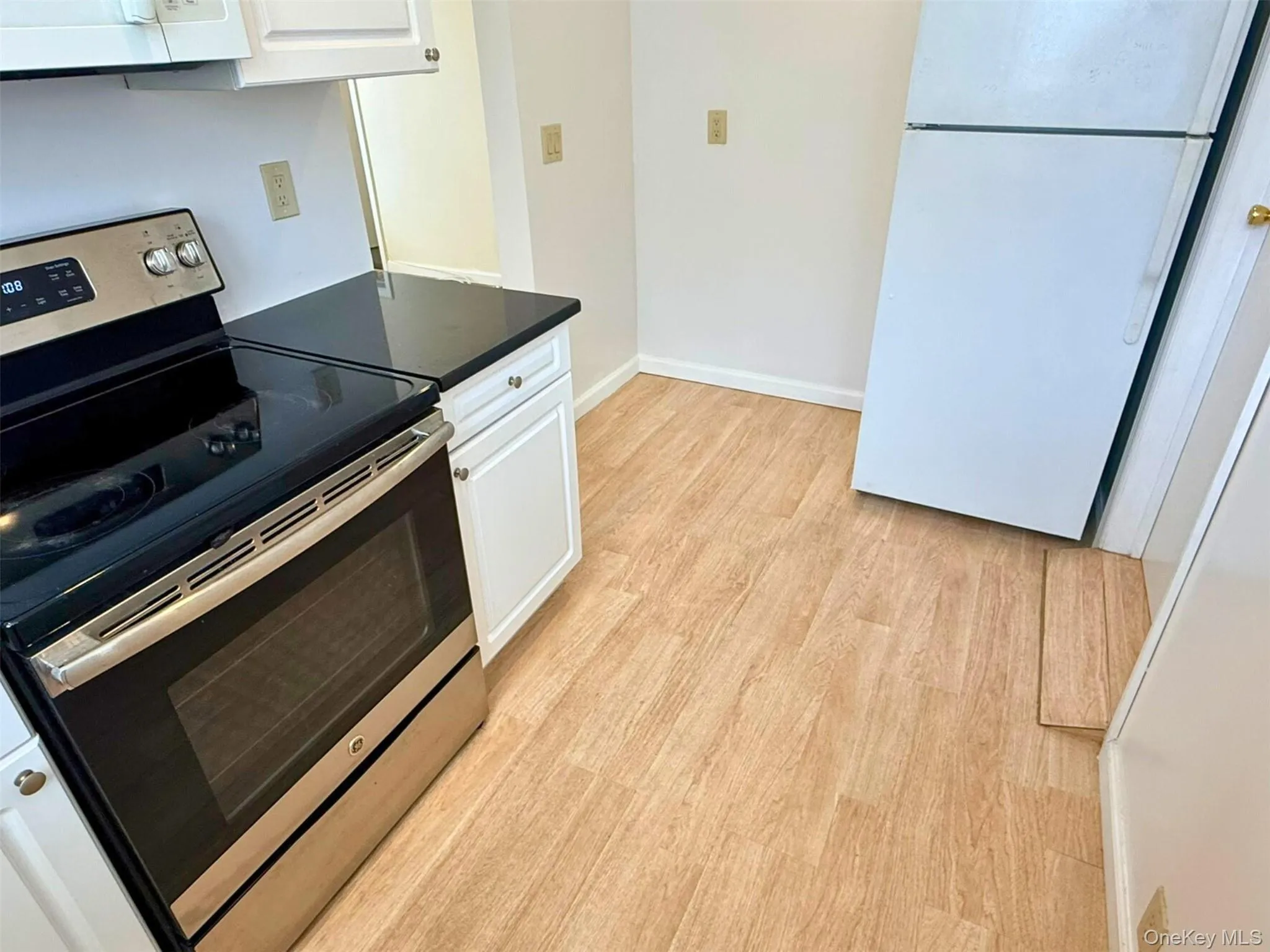 Kitchen featuring white appliances, dark countertops, light wood-type flooring, and white cabinetry Kitchen featuring white appliances, dark countertops, light wood-type flooring, and white cabinetry