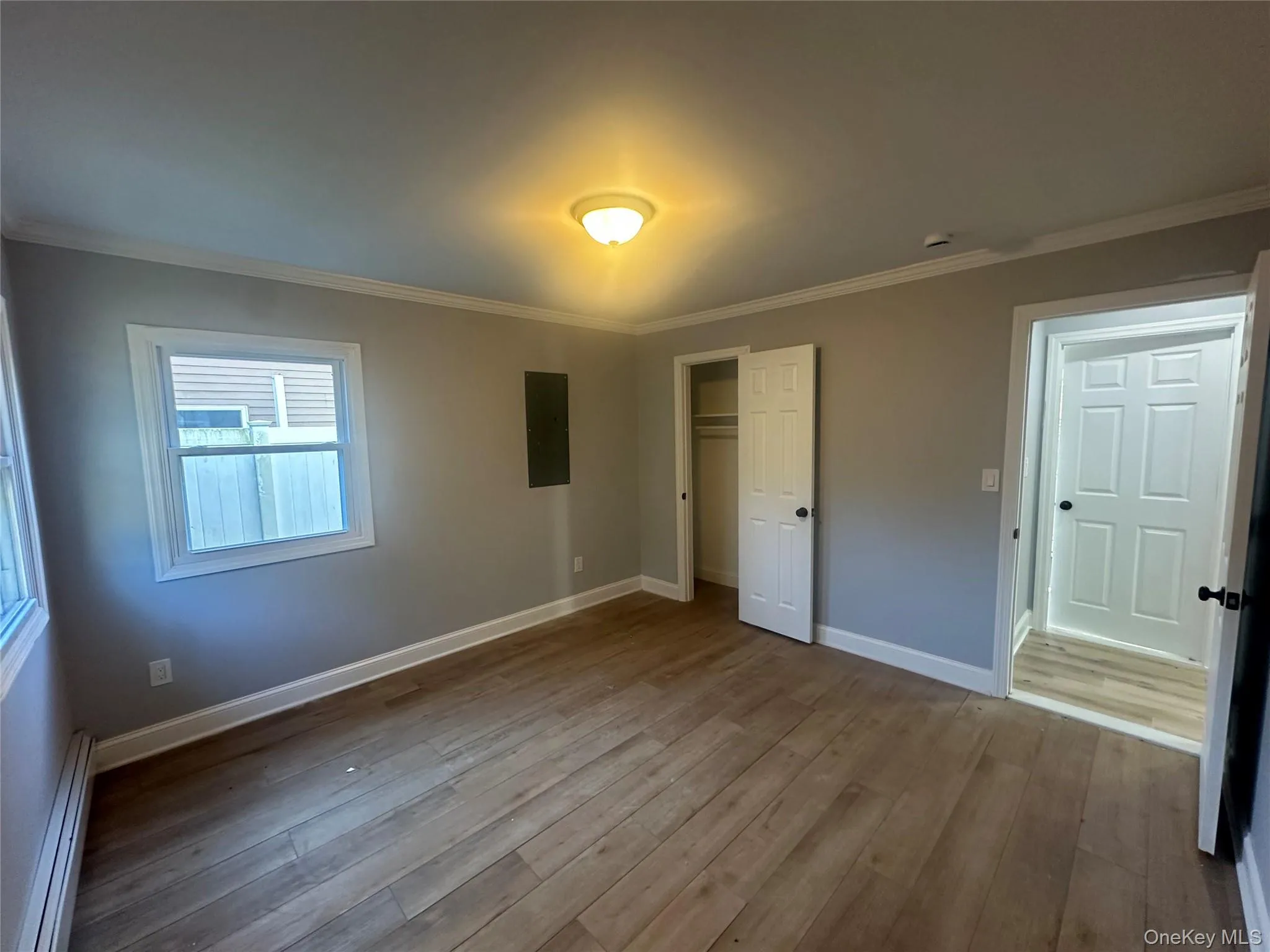 Unfurnished bedroom featuring baseboard heating, ornamental molding, a closet, hardwood / wood-style flooring, and electric panel Unfurnished bedroom featuring baseboard heating, ornamental molding, a closet, hardwood / wood-style flooring, and electric panel