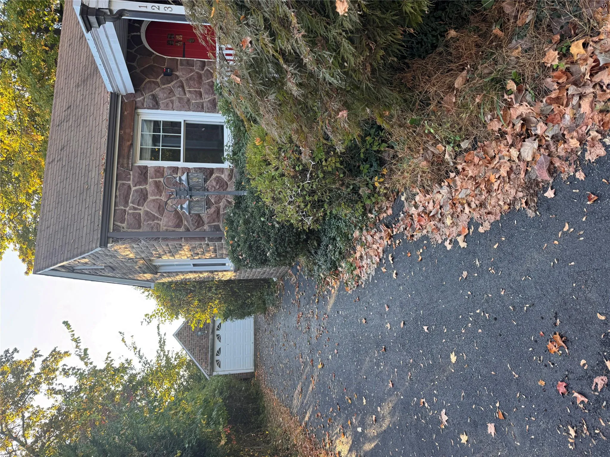 View of side of home with stone siding, an outdoor structure, and roof with shingles View of side of home with stone siding, an outdoor structure, and roof with shingles