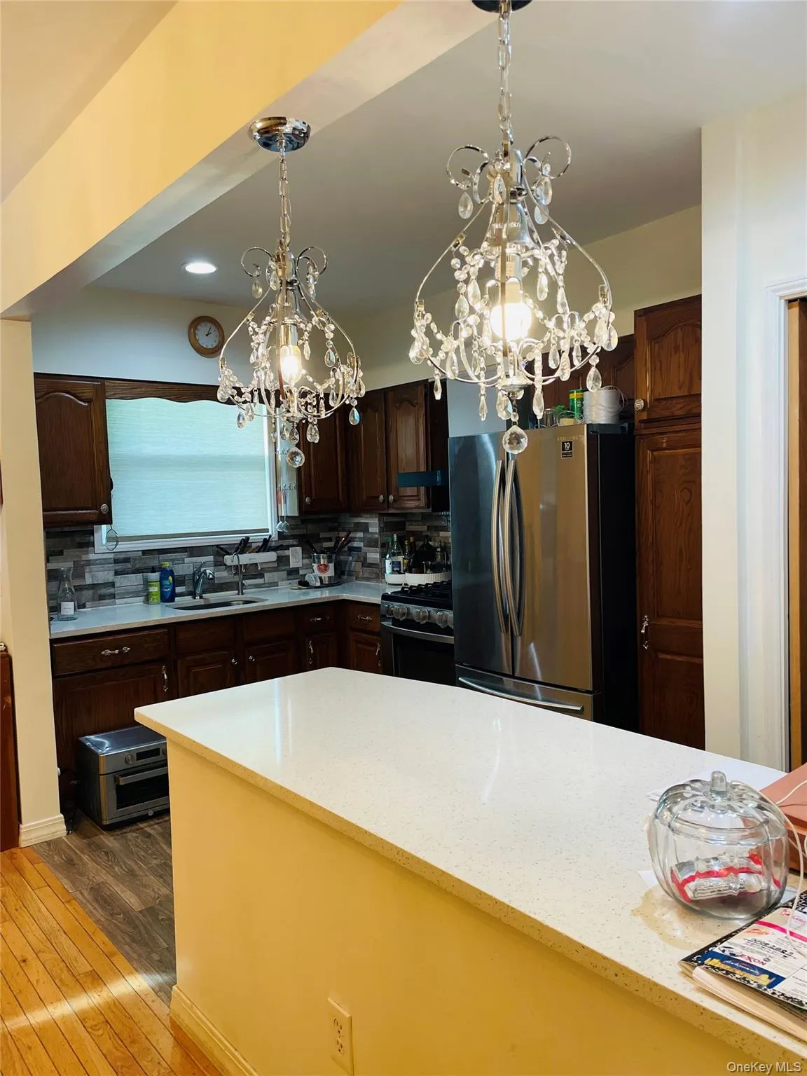 Kitchen with a chandelier, freestanding refrigerator, dark brown cabinetry, light stone counters, and recessed lighting Kitchen with a chandelier, freestanding refrigerator, dark brown cabinetry, light stone counters, and recessed lighting