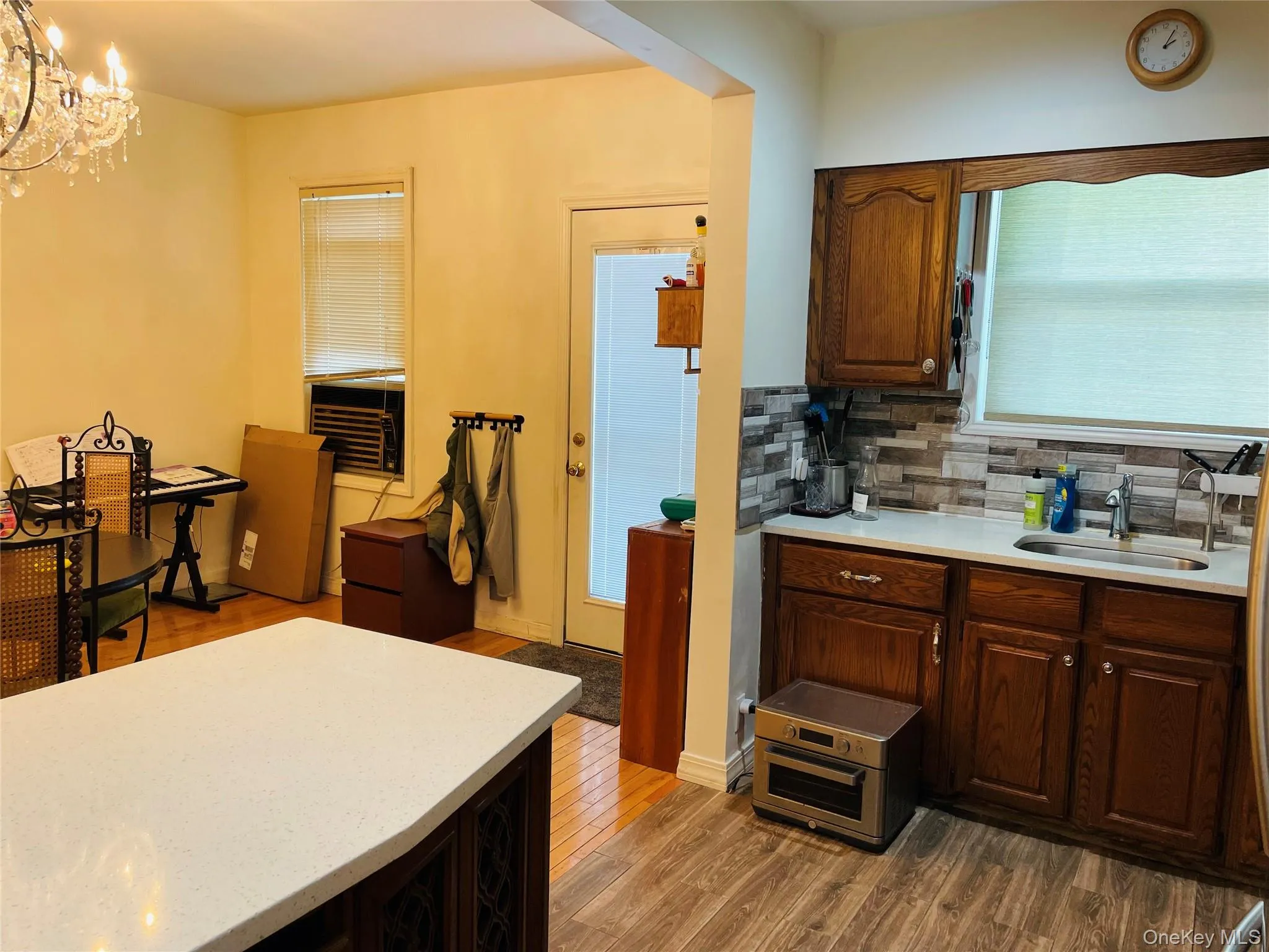 Kitchen featuring light stone countertops, dark wood finished floors, a chandelier, decorative backsplash, and hanging light fixtures Kitchen featuring light stone countertops, dark wood finished floors, a chandelier, decorative backsplash, and hanging light fixtures