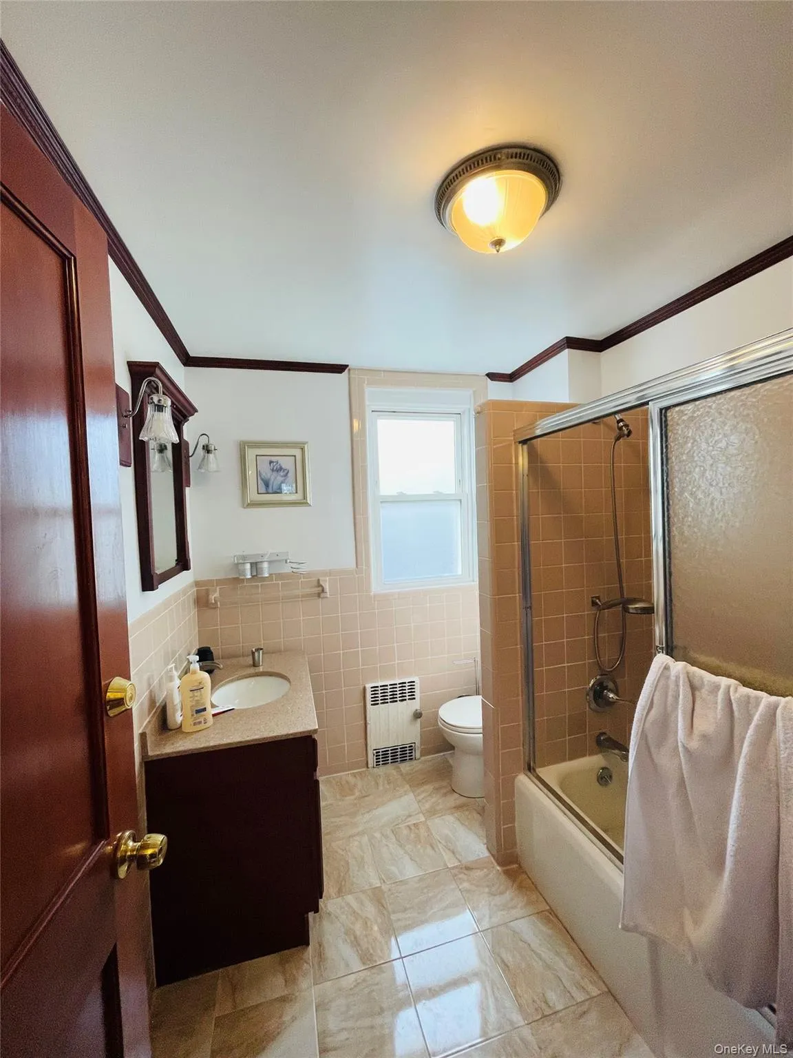 Full bath with vanity, ornamental molding, combined bath / shower with glass door, tile walls, and radiator Full bath with vanity, ornamental molding, combined bath / shower with glass door, tile walls, and radiator