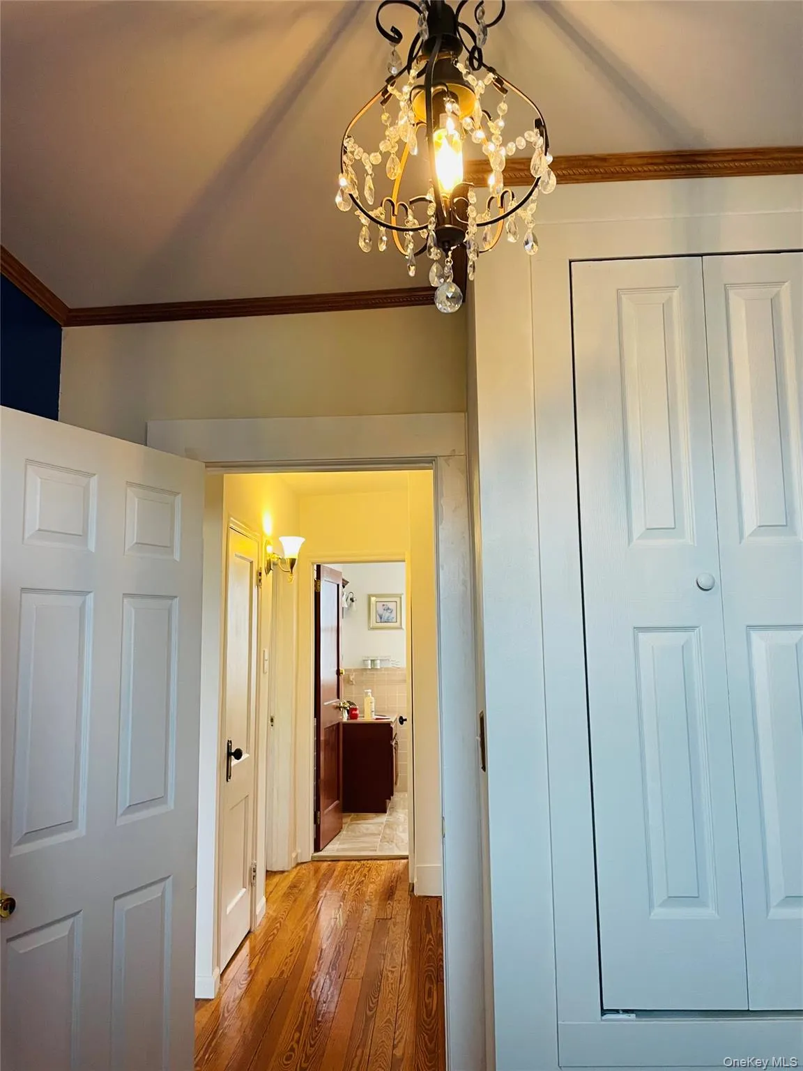 Corridor featuring crown molding, wood-type flooring, and a chandelier Corridor featuring crown molding, wood-type flooring, and a chandelier