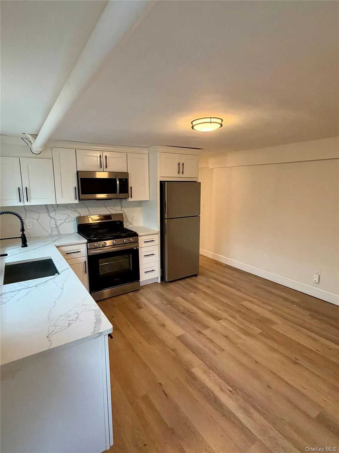 Kitchen with stainless steel appliances, white cabinets, backsplash, light stone countertops, and light wood finished floors. Kitchen with stainless steel appliances, white cabinets, backsplash, light stone countertops, and light wood finished floors.