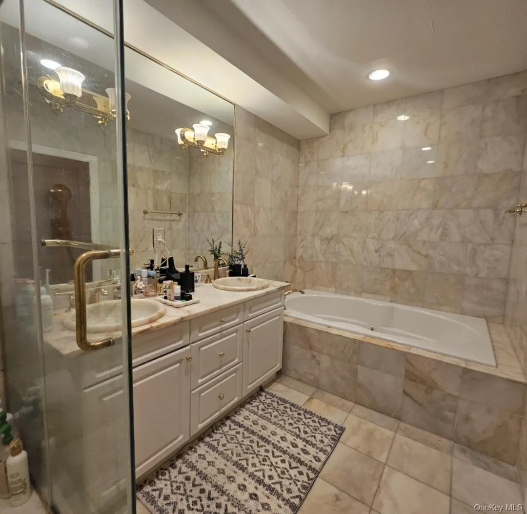 Bathroom with double vanity, tile walls, a bath, a stall shower, and a chandelier Bathroom with double vanity, tile walls, a bath, a stall shower, and a chandelier