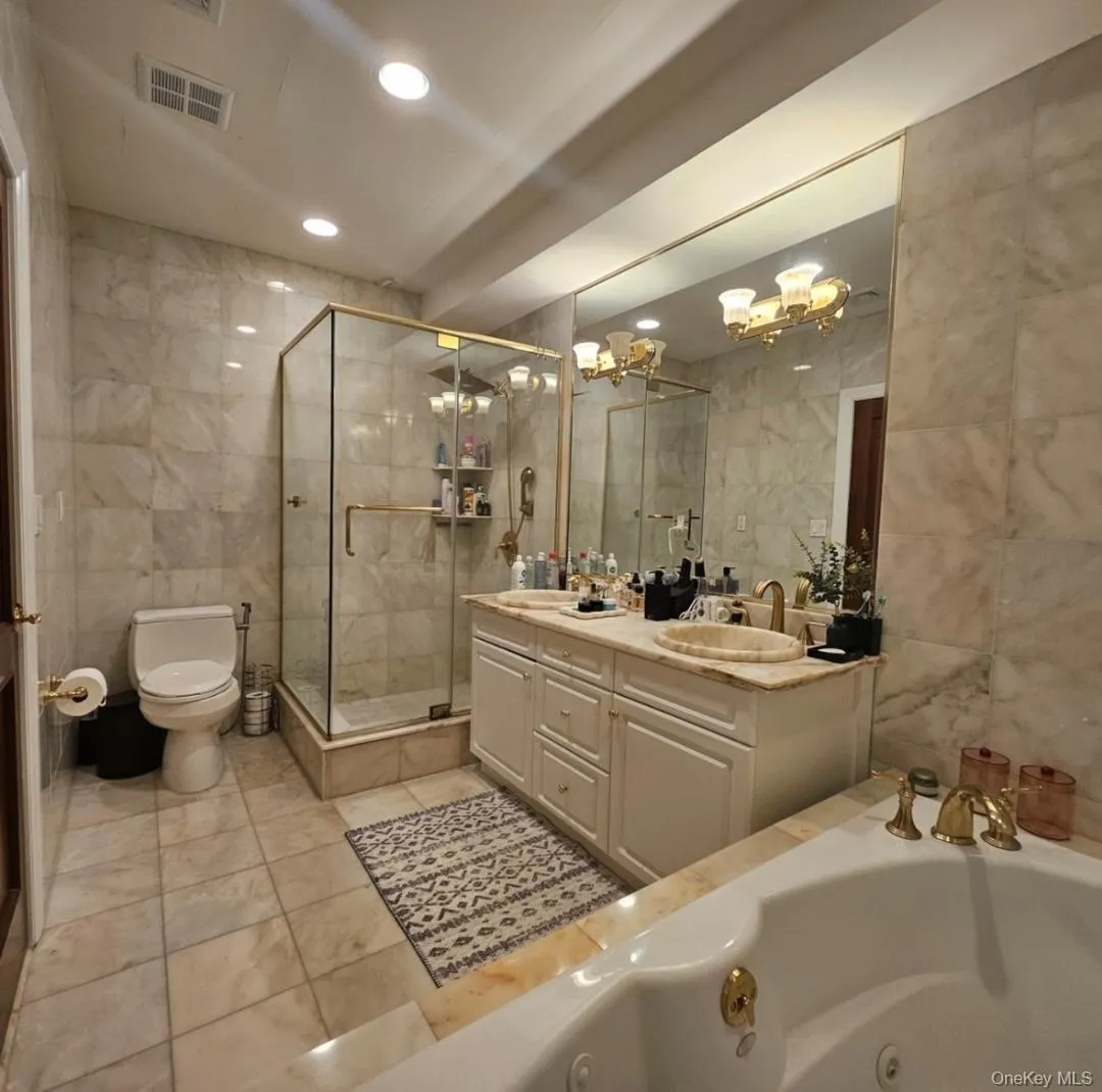Bathroom featuring tile walls, double vanity, a jetted tub, a chandelier, and a stall shower Bathroom featuring tile walls, double vanity, a jetted tub, a chandelier, and a stall shower