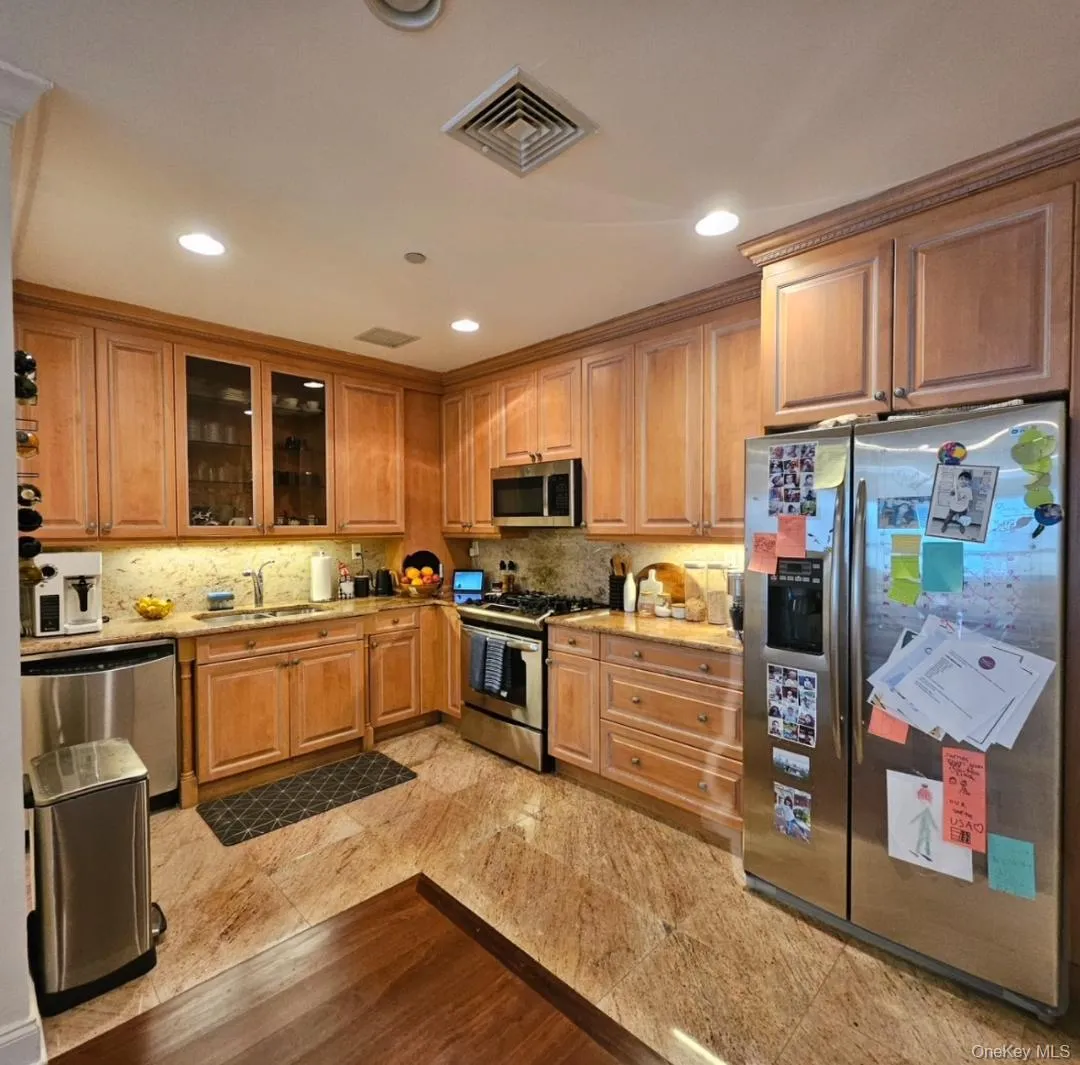 Kitchen featuring stainless steel appliances, light stone countertops, glass insert cabinets, tasteful backsplash, and recessed lighting Kitchen featuring stainless steel appliances, light stone countertops, glass insert cabinets, tasteful backsplash, and recessed lighting