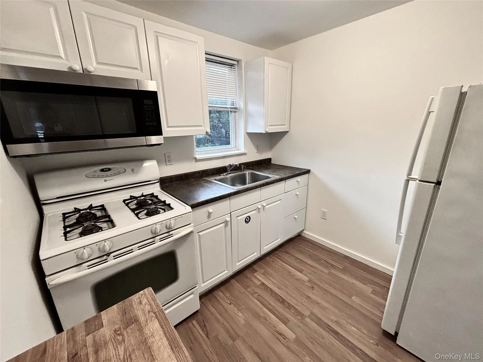 Kitchen featuring white appliances, a sink, dark countertops, white cabinets, and wood finished floors Kitchen featuring white appliances, a sink, dark countertops, white cabinets, and wood finished floors