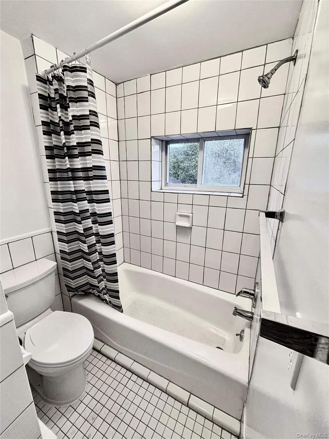 Bathroom with shower / bath combination with curtain, toilet, tile walls, tile patterned floors, and a wainscoted wall Bathroom with shower / bath combination with curtain, toilet, tile walls, tile patterned floors, and a wainscoted wall