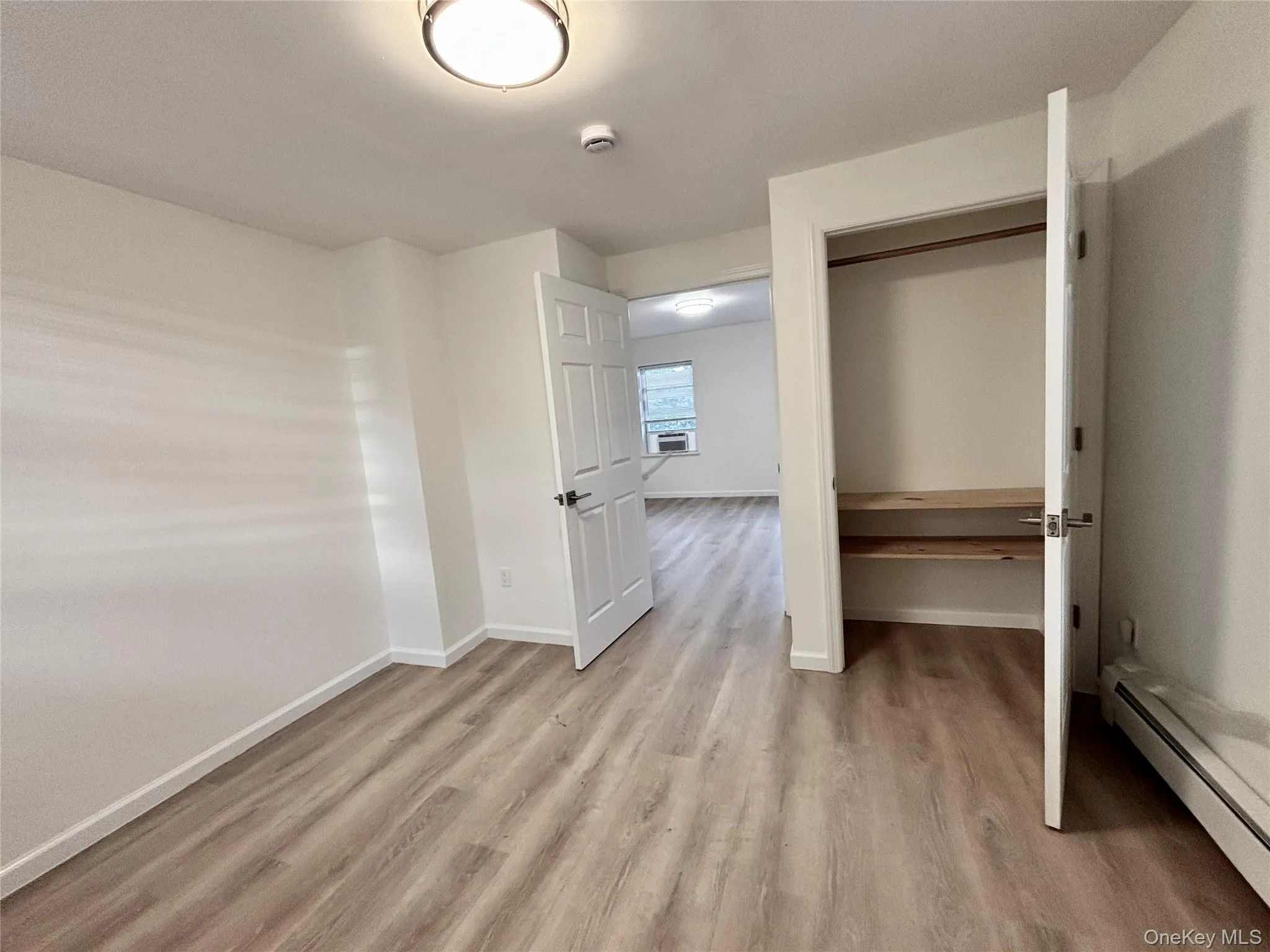 Unfurnished bedroom with a baseboard radiator, light wood-type flooring, baseboards, and a closet Unfurnished bedroom with a baseboard radiator, light wood-type flooring, baseboards, and a closet