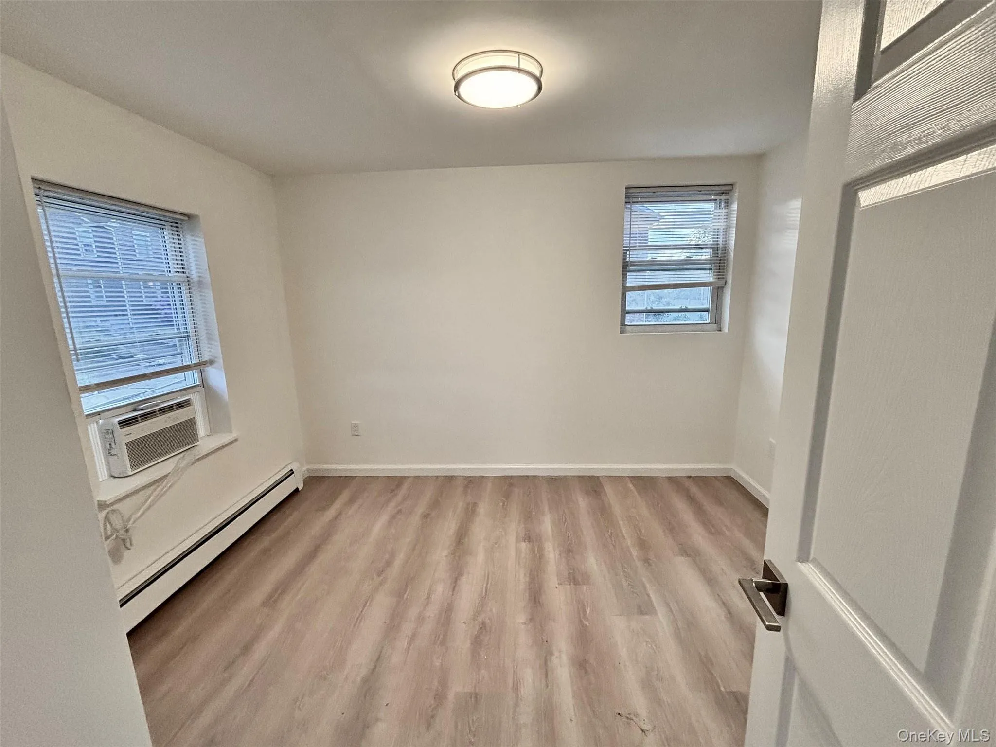 Spare room featuring a baseboard radiator, light wood-type flooring, baseboards, and cooling unit Spare room featuring a baseboard radiator, light wood-type flooring, baseboards, and cooling unit