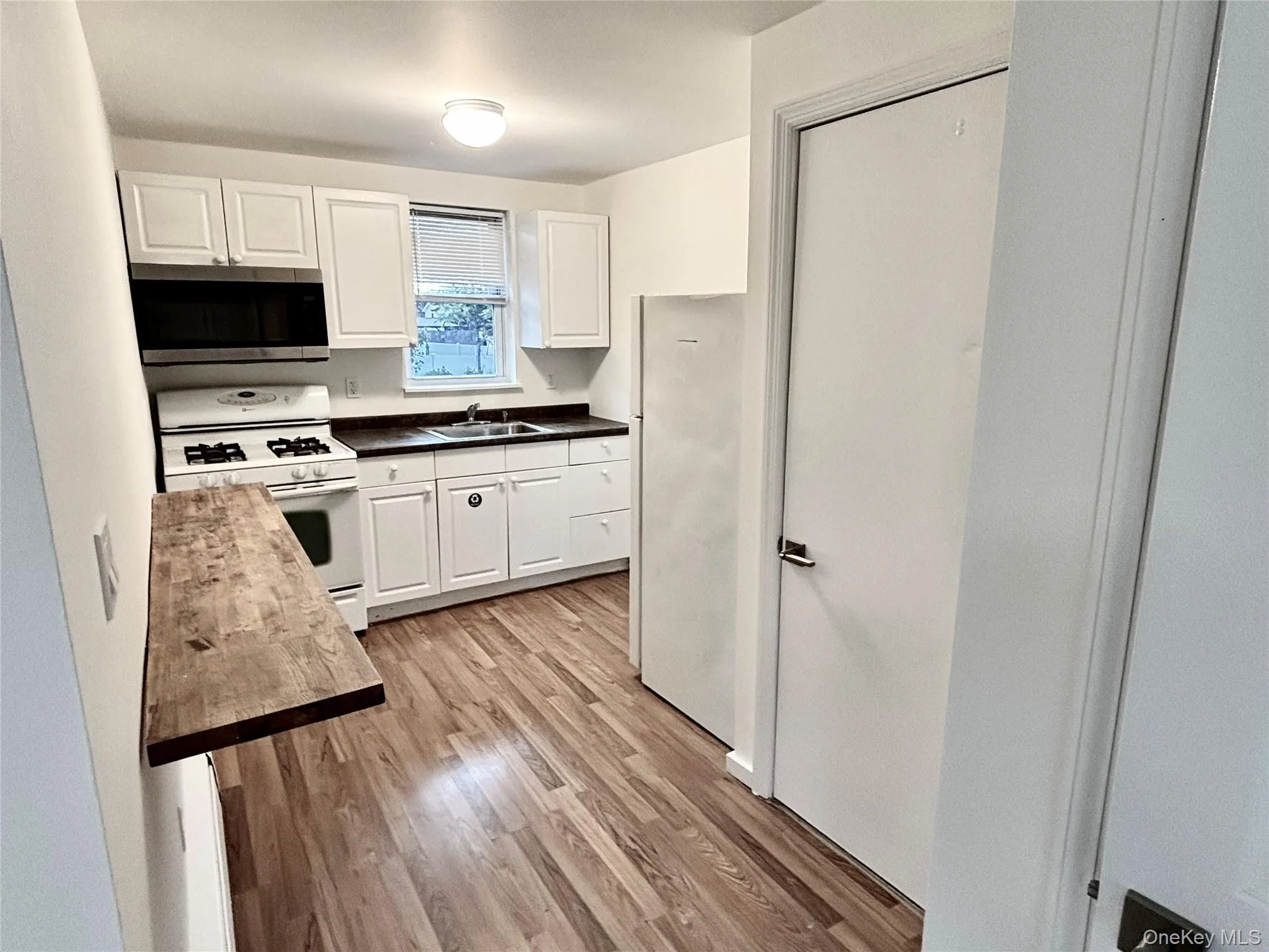 Kitchen with white appliances, a sink, light wood finished floors, white cabinets, and dark countertops Kitchen with white appliances, a sink, light wood finished floors, white cabinets, and dark countertops
